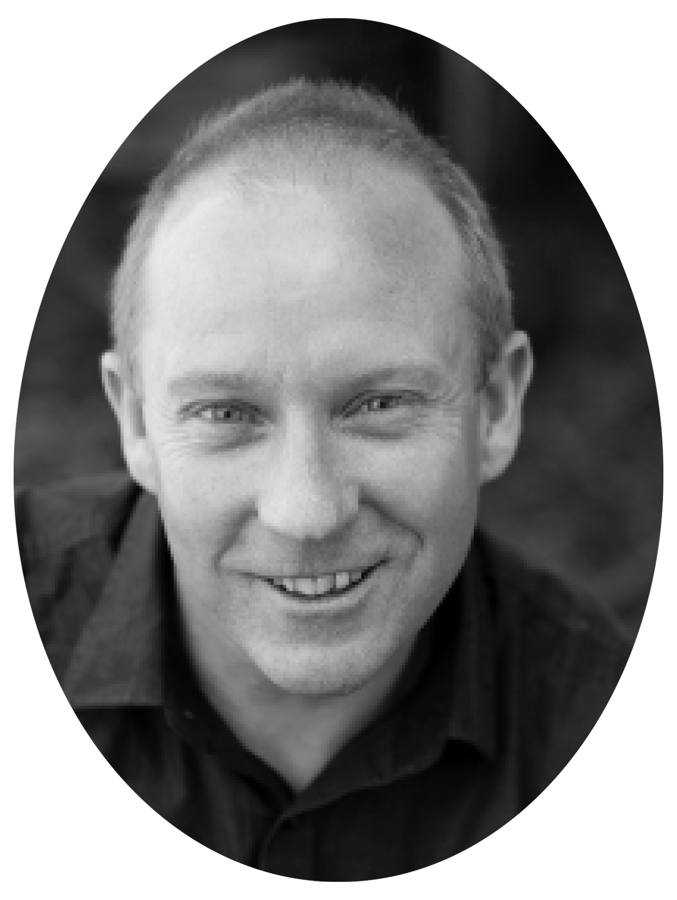 Black and white close-up photo of a smiling man with short hair, wearing a dark collared shirt.