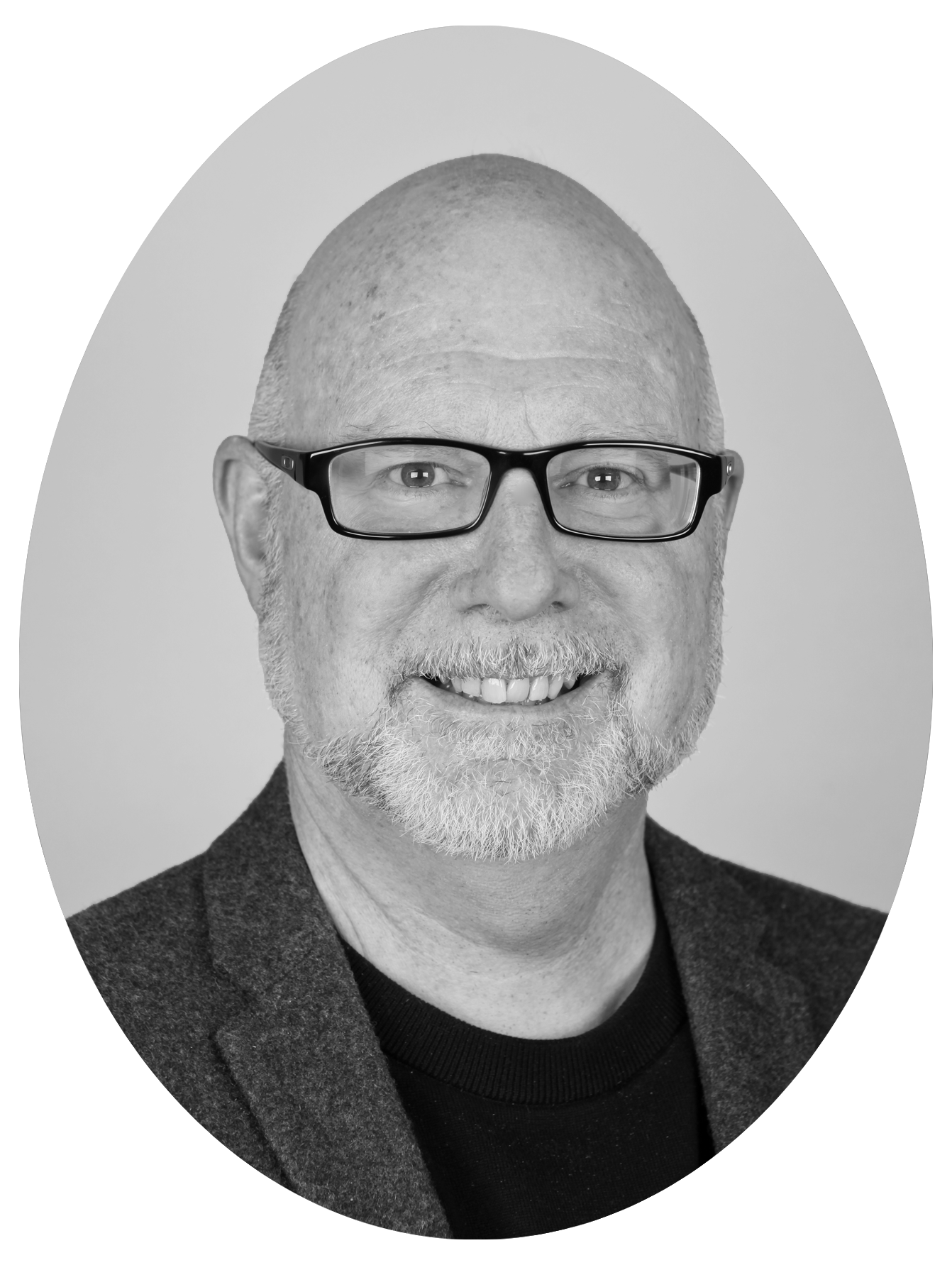 Black and white portrait of a middle-aged man with glasses, a beard, and a receding hairline, smiling, wearing a blazer over a sweater.