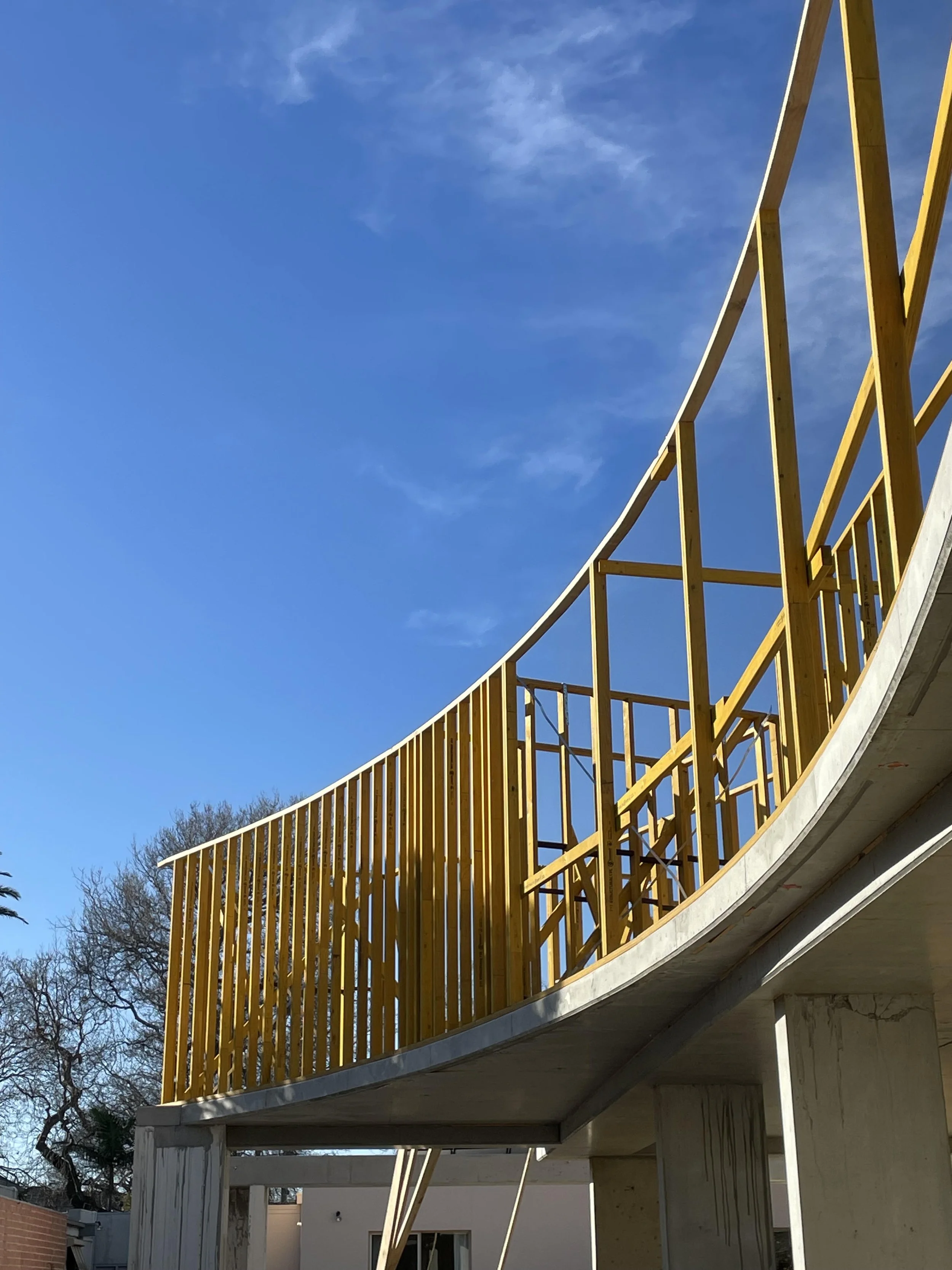 Construction site with a partially built concrete structure and yellow safety railing, under a blue sky with some clouds.