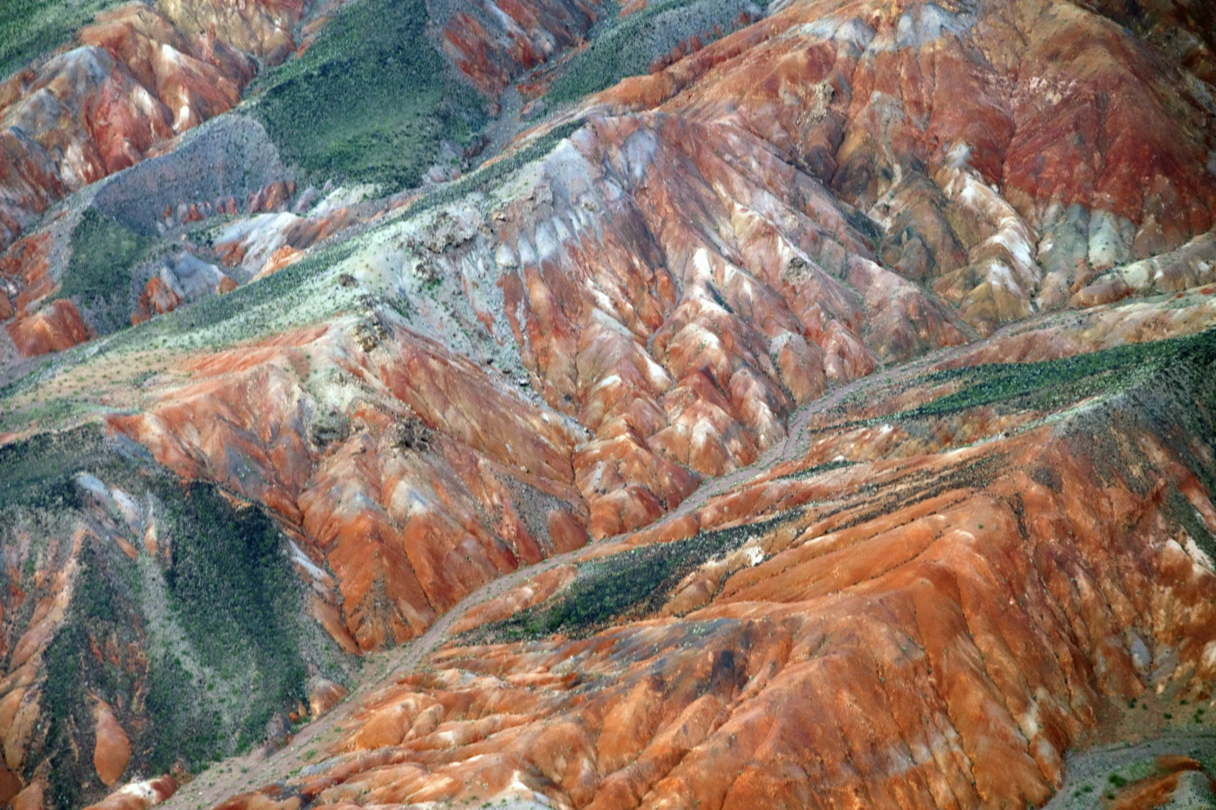 Colorful layered mountain landscape with red, white, green, and brown hues.
