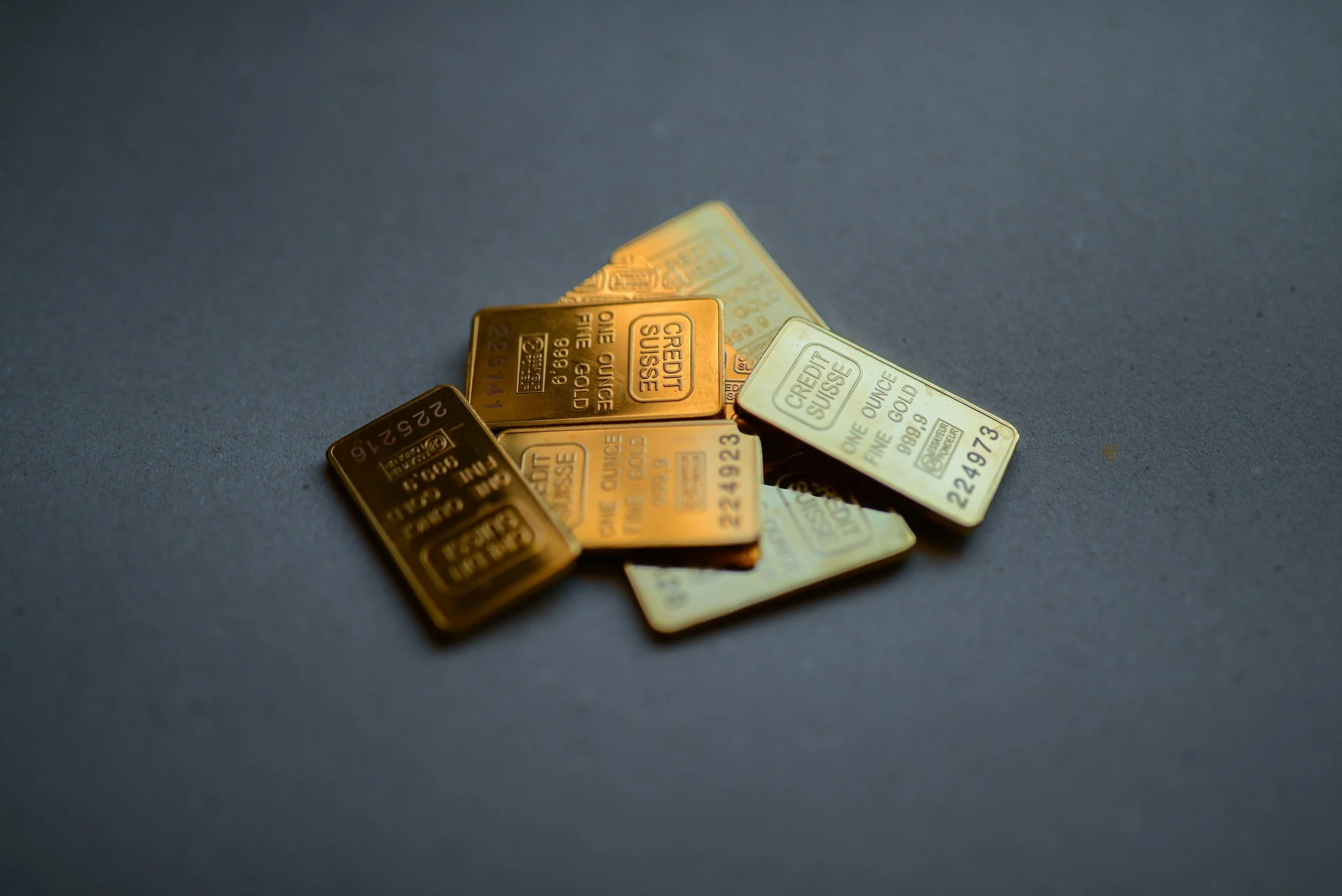 Several small gold and silver bars on a dark surface, with some overlapping each other.