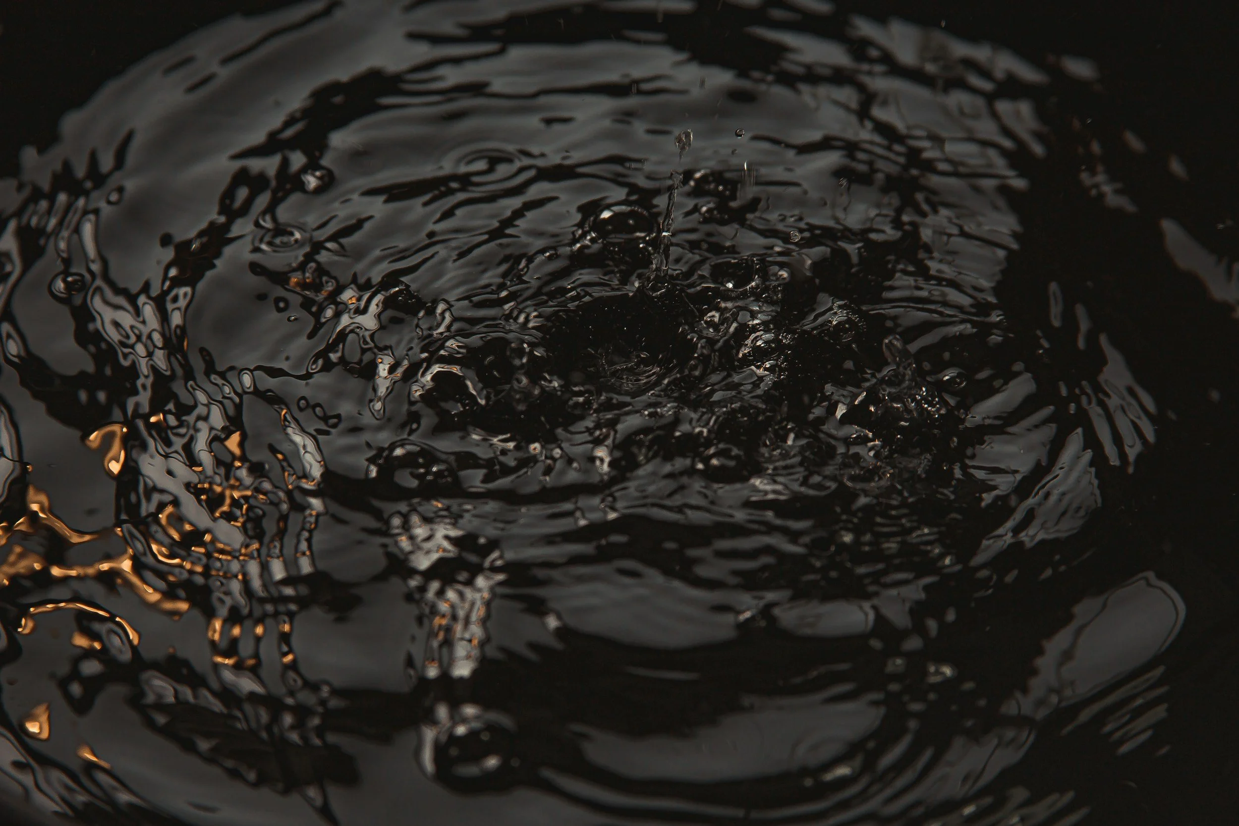 Close-up of black liquid rippling and splashing in water.