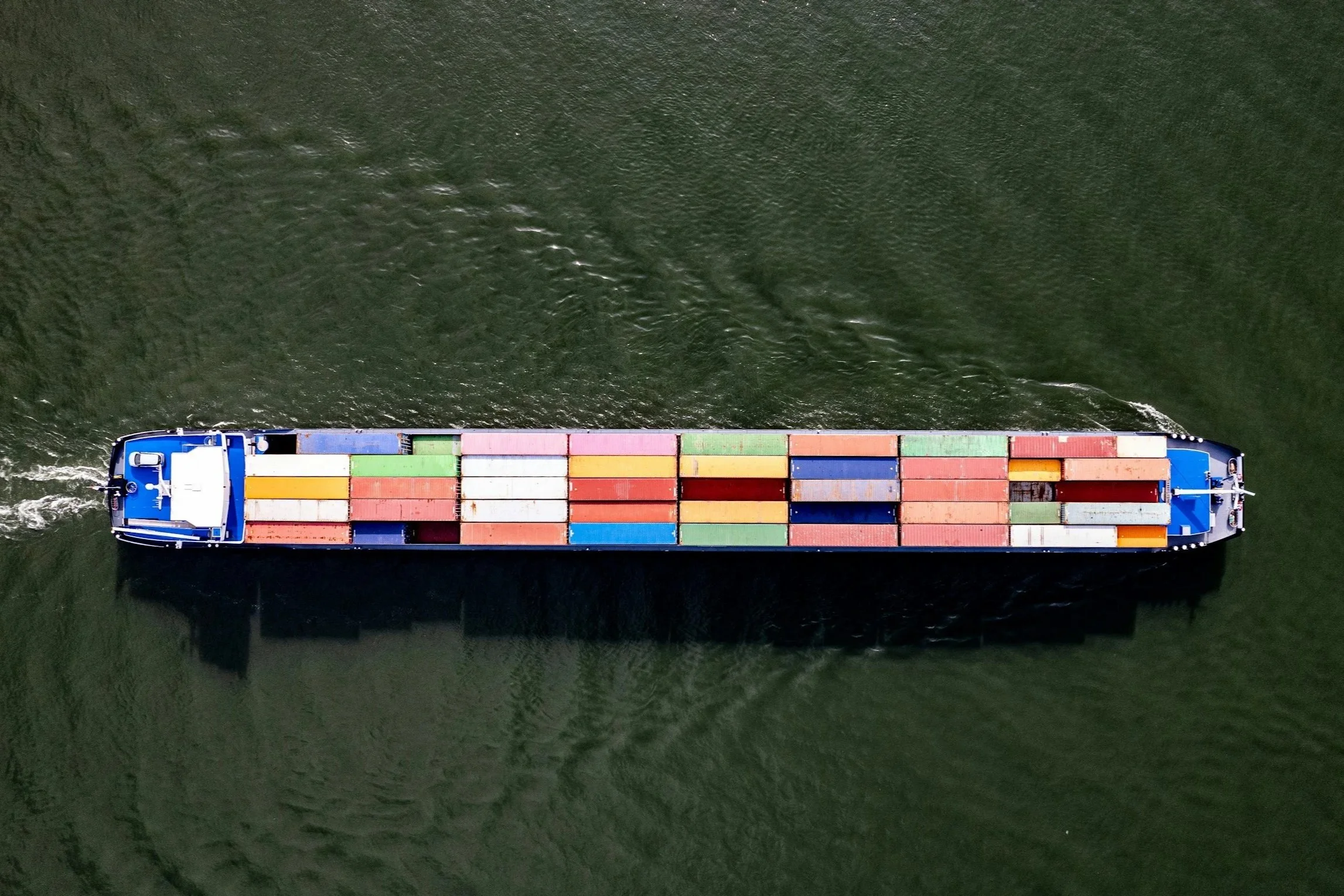 An aerial view of a large cargo ship with colorful containers sailing on dark green water.