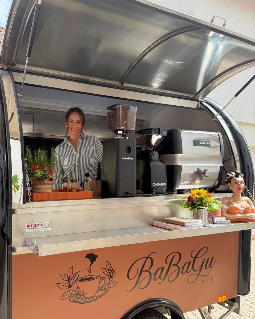 Barbara serviert Kaffee am geöffneten Fenster des BaBaGu Kaffee-Trailers