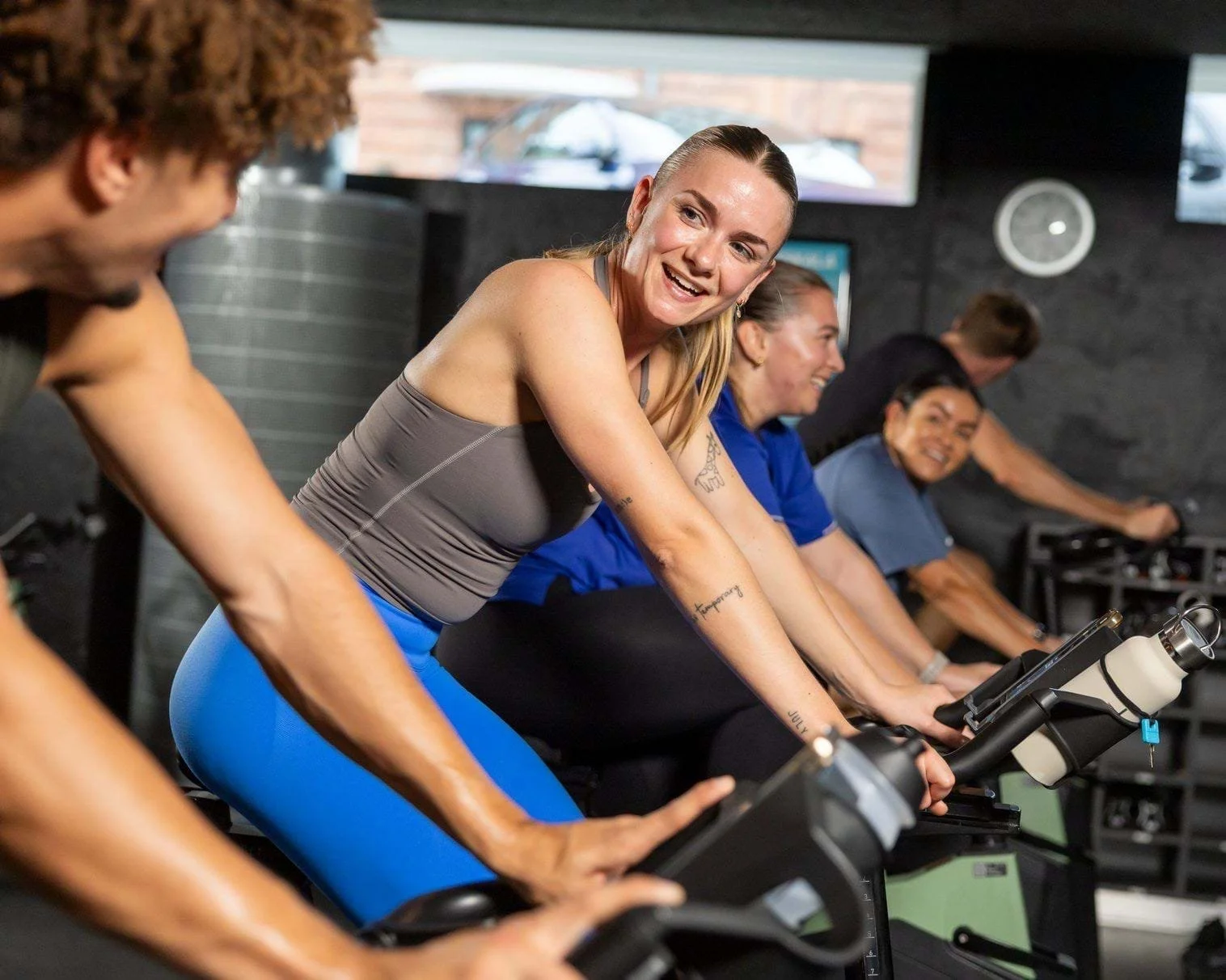 People spinning on stationary bikes during an indoor cycling class at a gym.