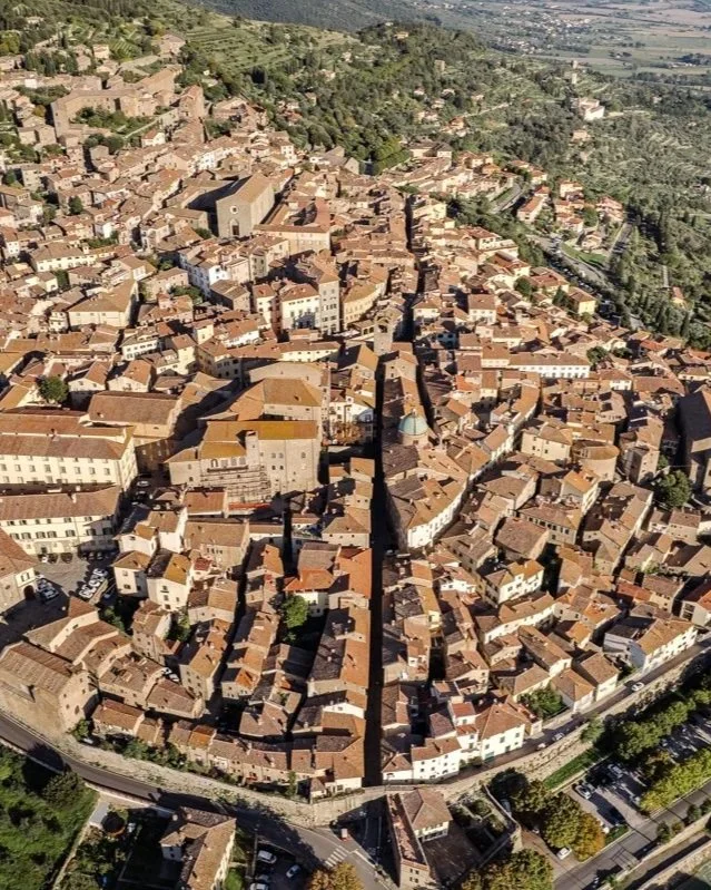 Aerial view of a historic European city with narrow streets, terracotta rooftops, and ancient stone buildings surrounded by greenery.
