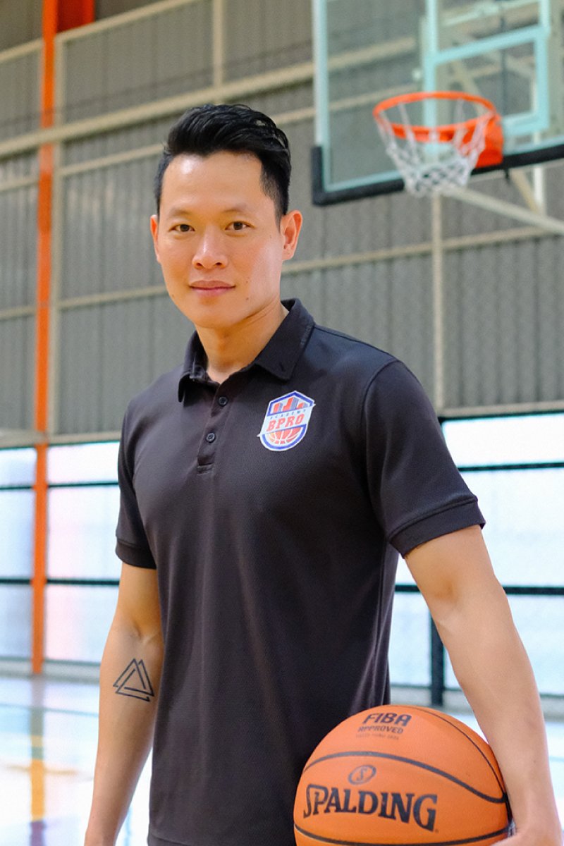 A young man with short black hair holding a basketball in a gymnasium.