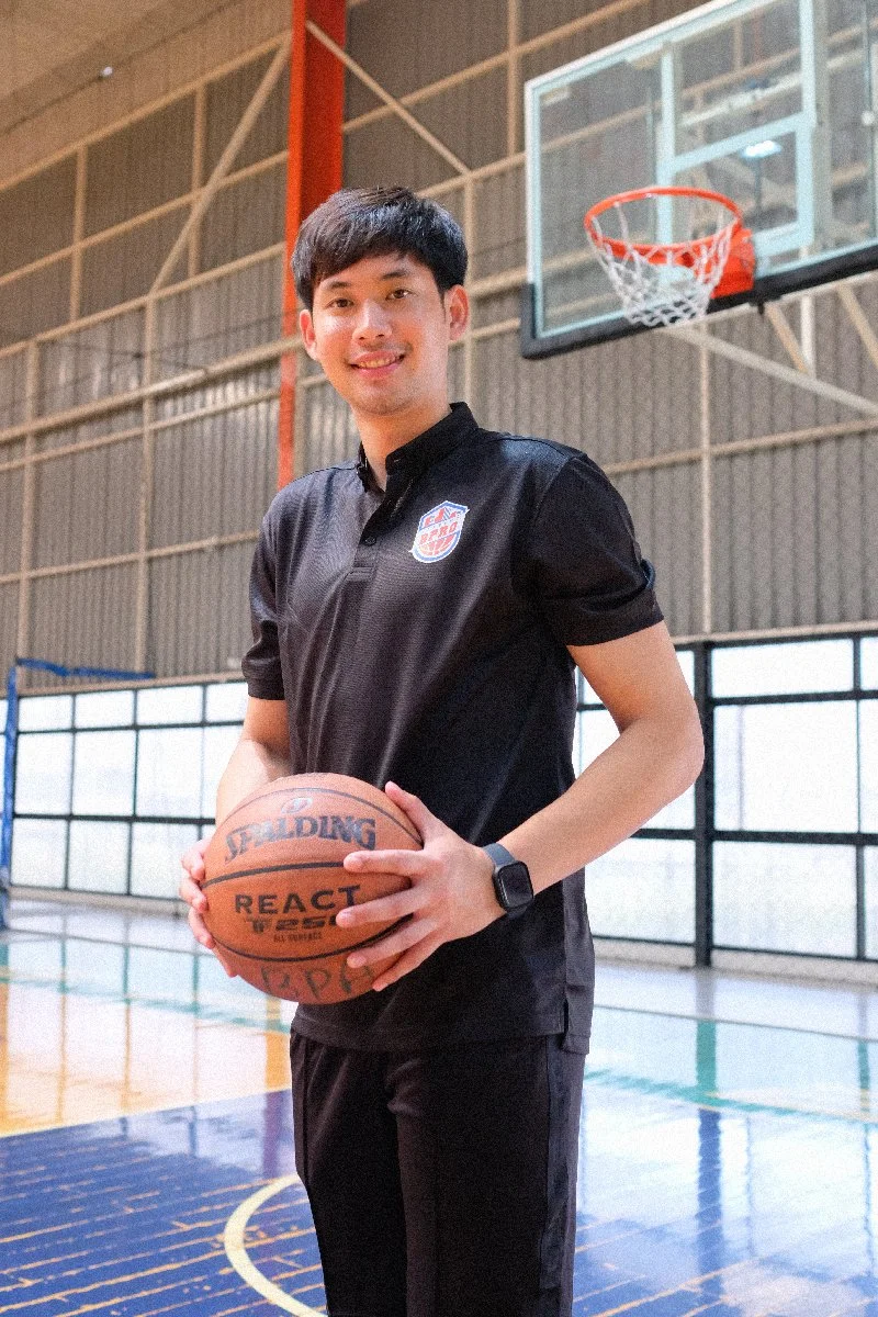 A young man in a black sports shirt holding a basketball inside a basketball court.