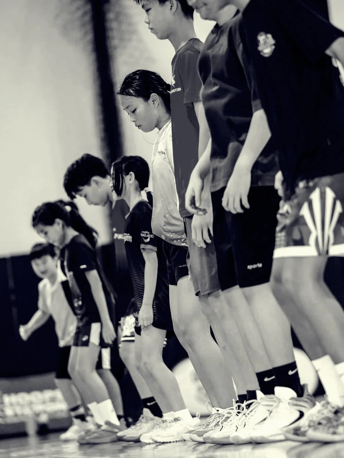 Group of young athletes standing in a line, bowing their heads in a moment of silence or prayer.