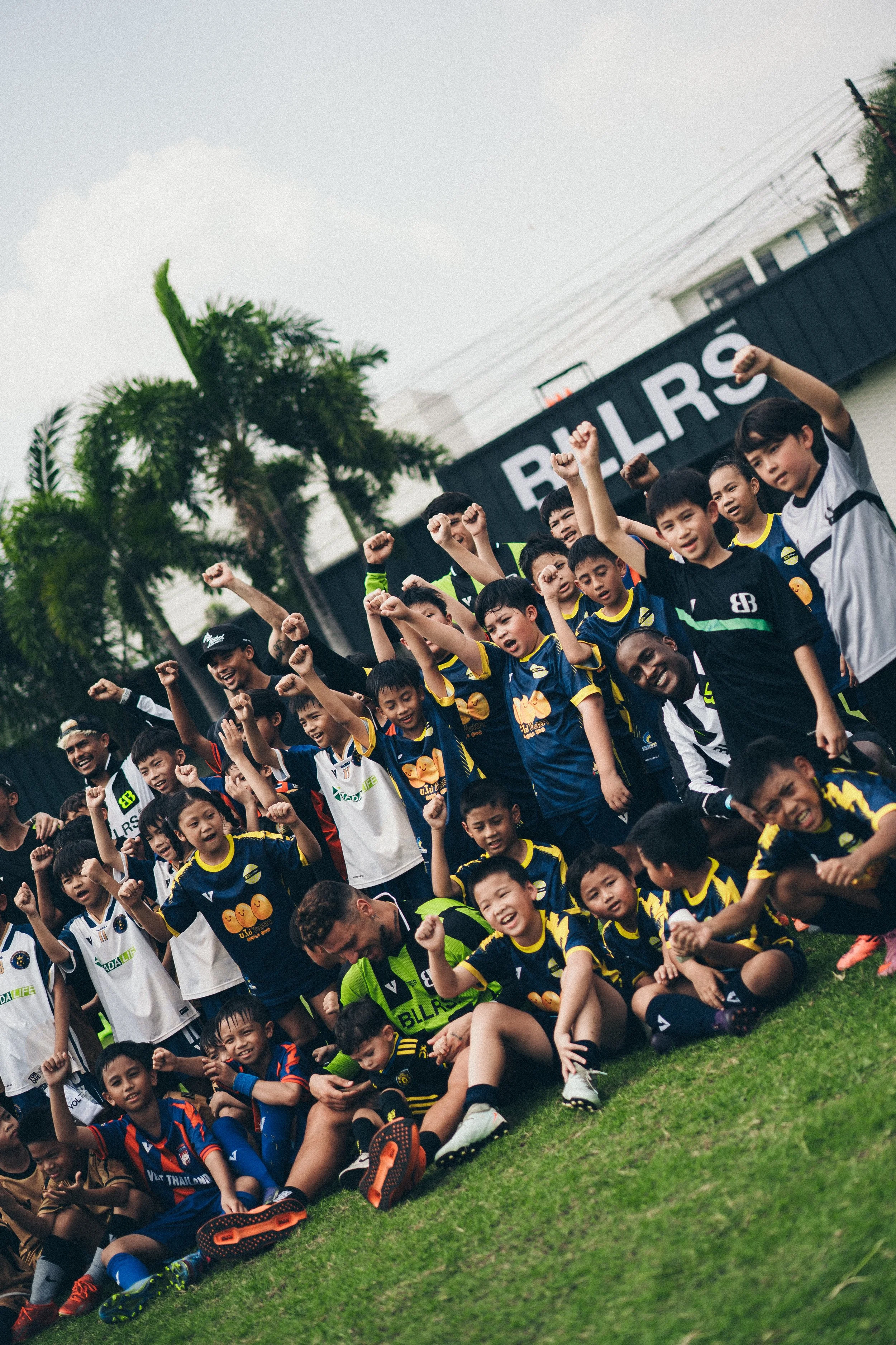 Group of children and adults celebrating on a sports field, raising their fists and smiling.