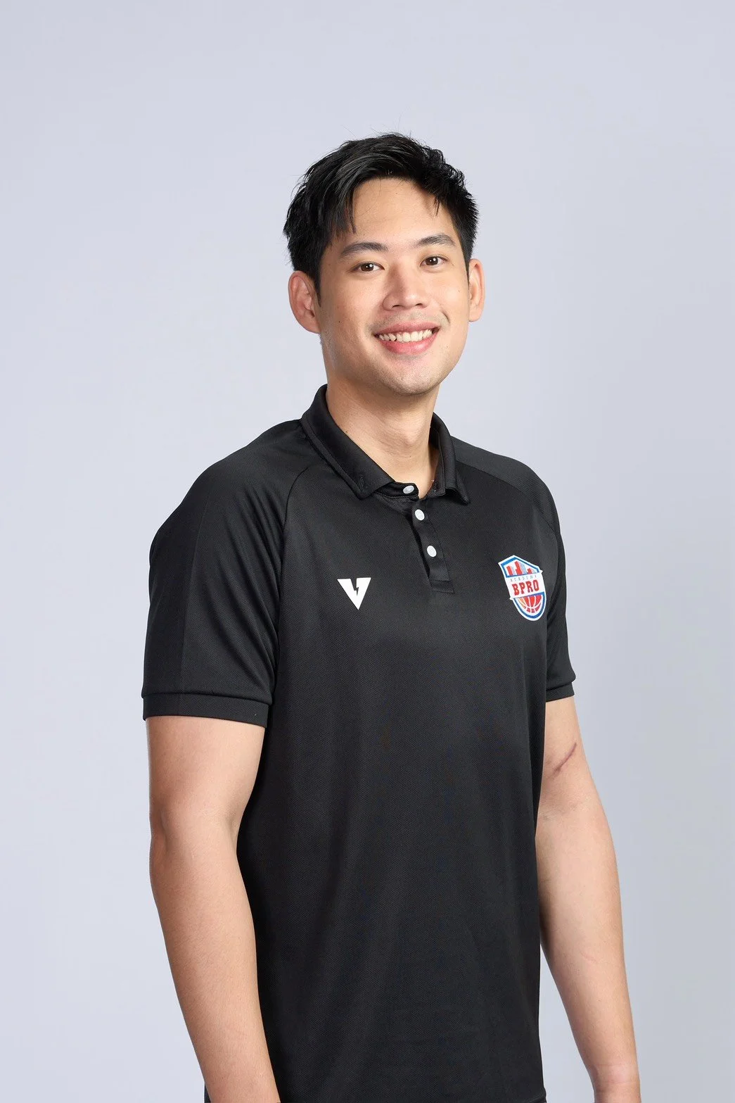 A young man in a black sports shirt holding a basketball inside a basketball court.