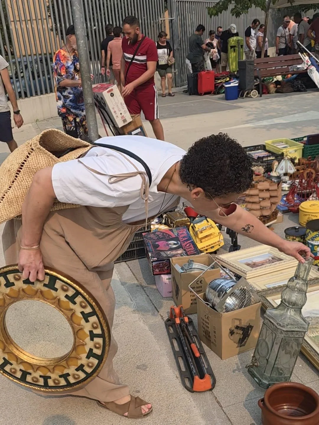 Anoa revisando artículos en una venta en el Rastro de Valencia, con muchas otras personas y objetos en el fondo.