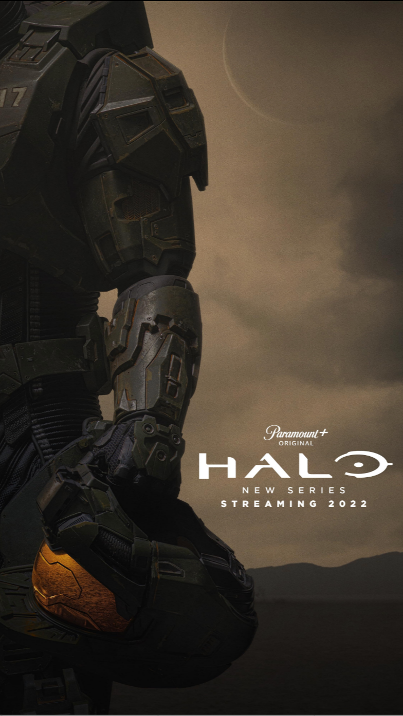 Poster for the game Halo featuring a close-up of a futuristic armored soldier holding a helmet, with mountains and cloudy sky in the background. Text on the poster reads 'Paramount+ Original Halo New Series Streaming 2022'.