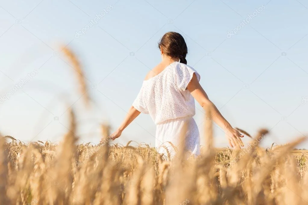 Frau in einem weißen Kleid geht durch einen Weizenfeld bei Sonnenuntergang.