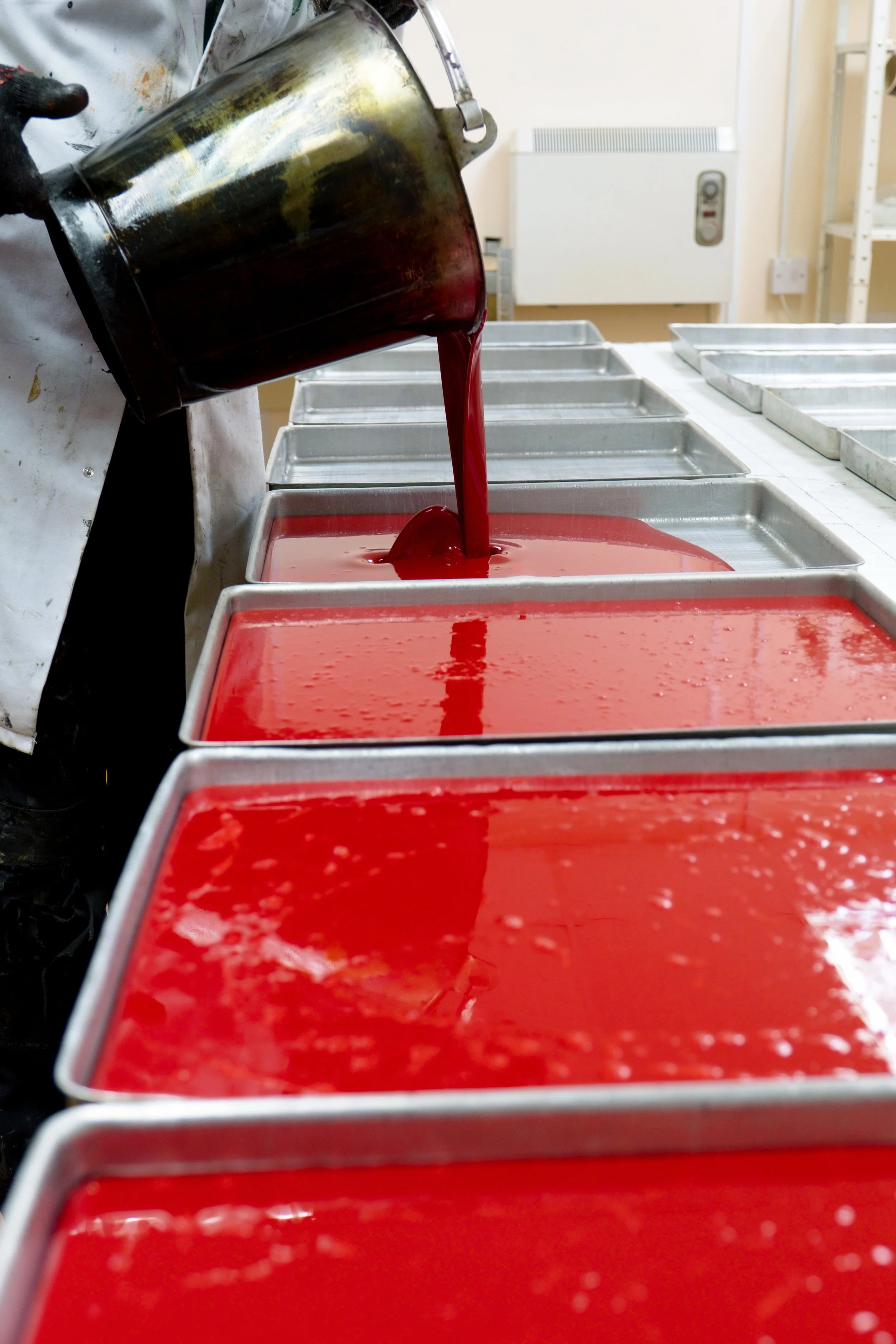 A person pouring red liquid into metal containers in a kitchen or food production area.
