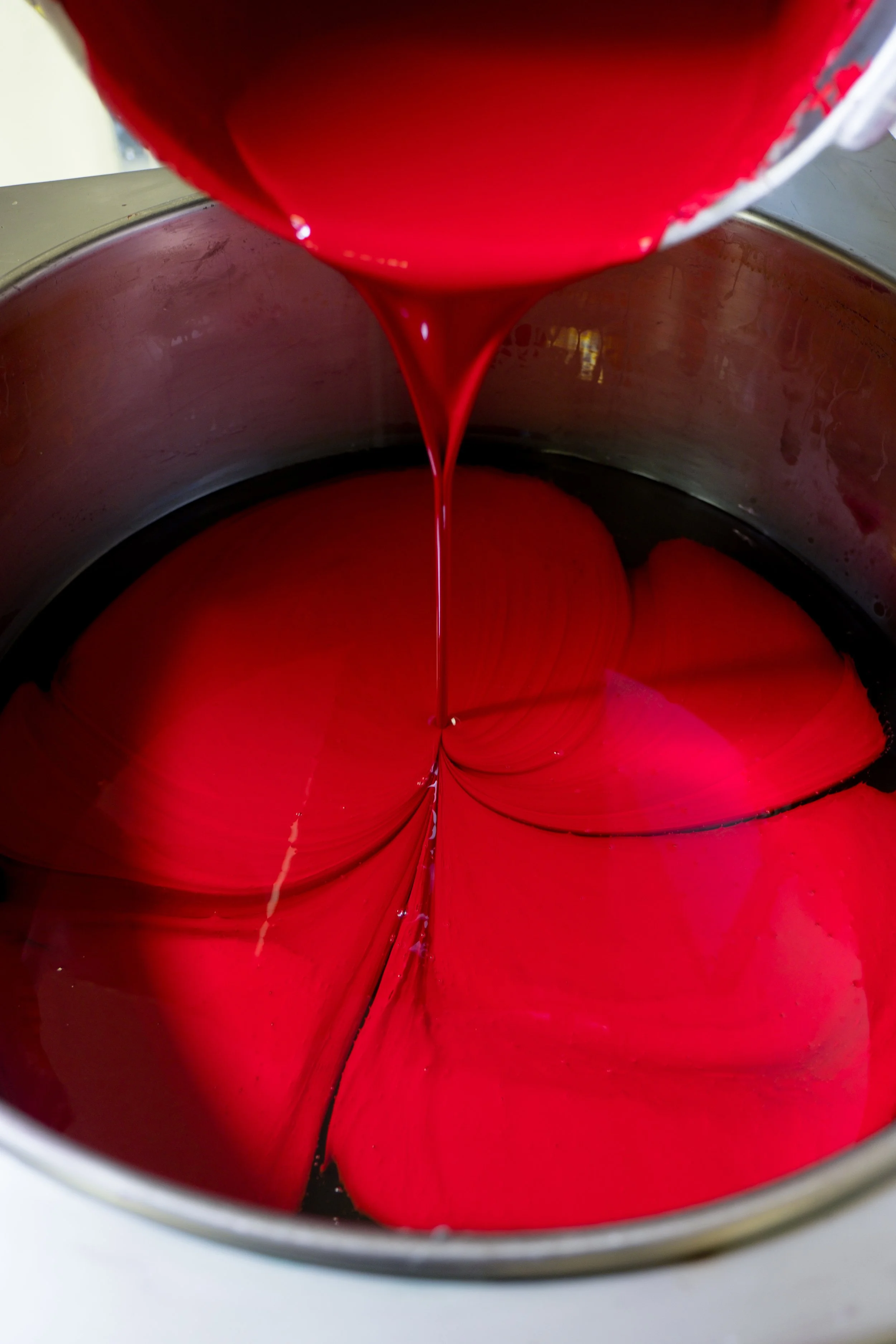 Red liquid being poured into a metal container, creating swirling patterns inside.