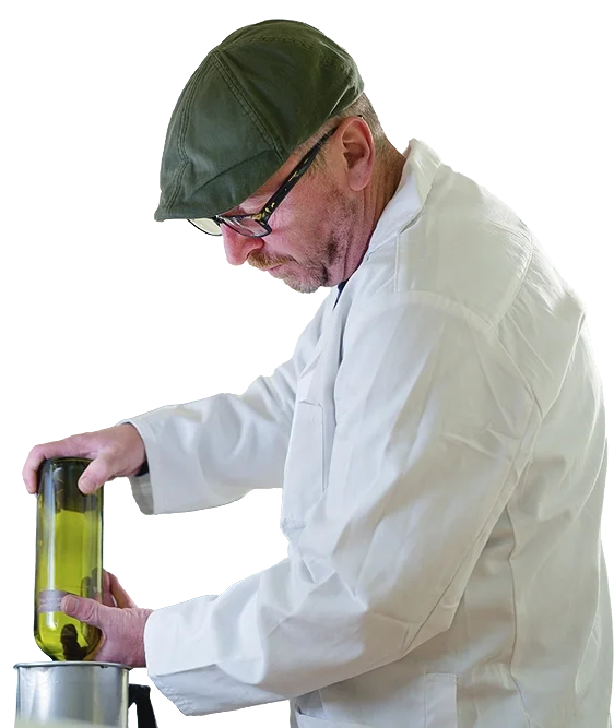 A man in a white lab coat and green cap performing an experiment with a test tube containing yellow liquid in a laboratory.