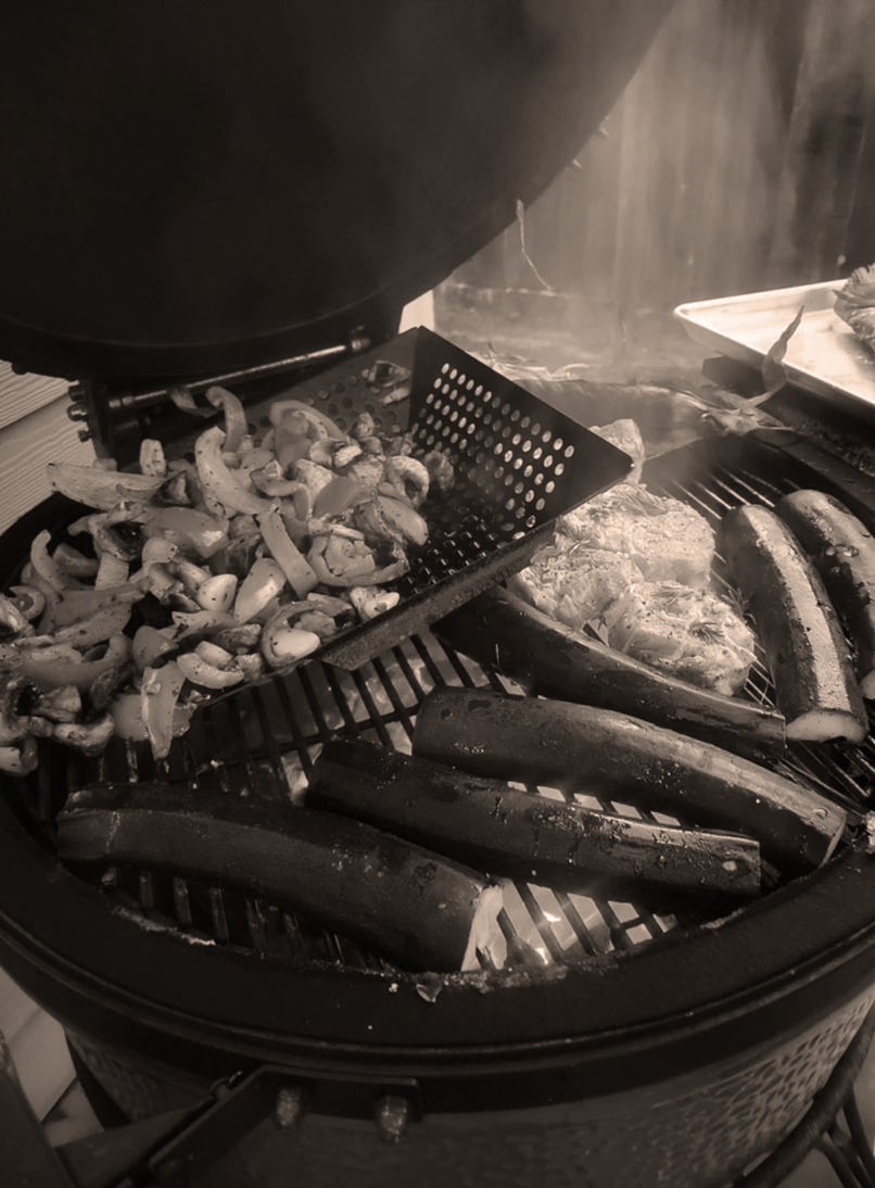 Vegetables and meats being grilled in an outdoor barbecue grill.