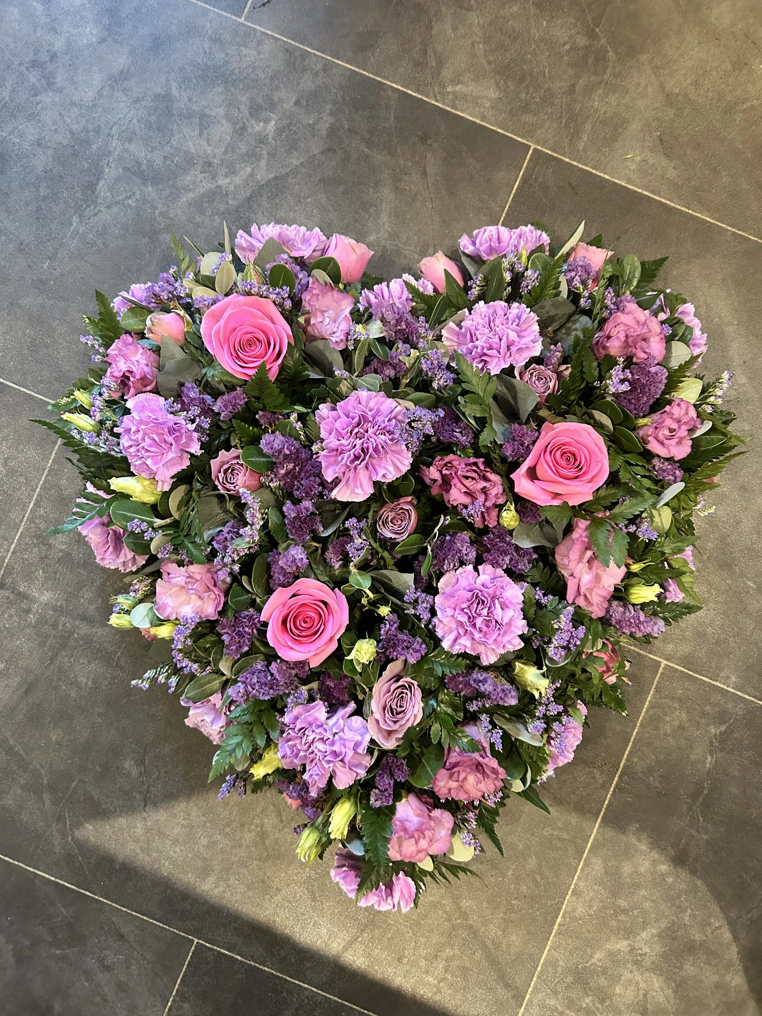 A large floral arrangement with pink roses, purple carnations, and greenery placed on a dark tile floor.