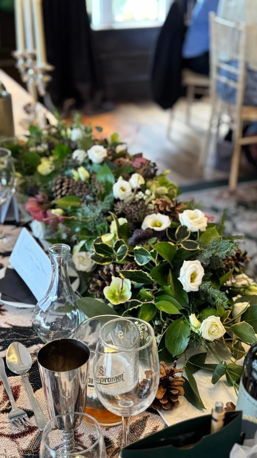 A table decorated with a lush floral centerpiece, wine glasses, a carafe, and cutlery, set for a formal meal in a cozy, rustic indoor setting.