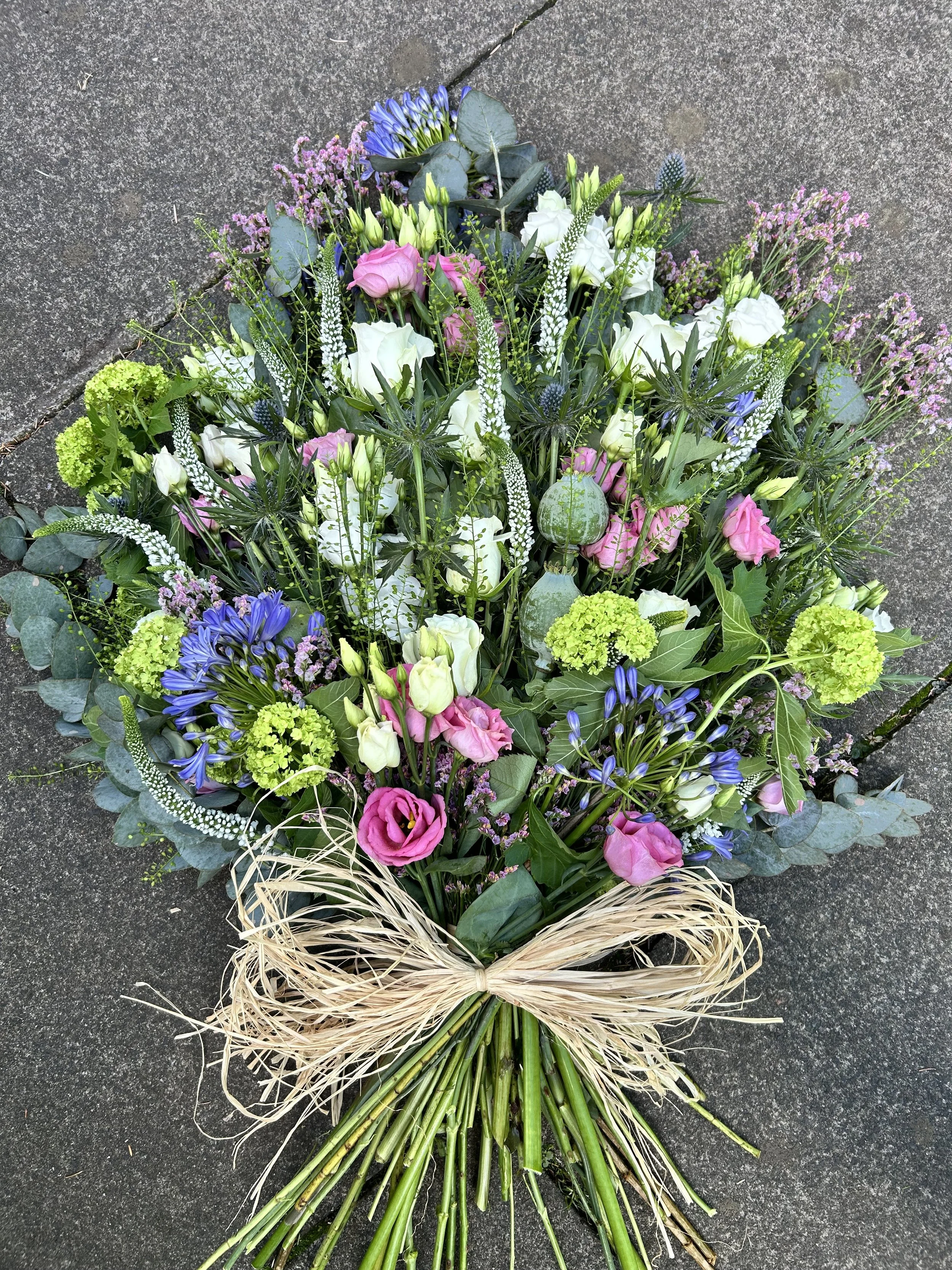 A bouquet of assorted fresh flowers on a dark ground, tied with a natural raffia ribbon.