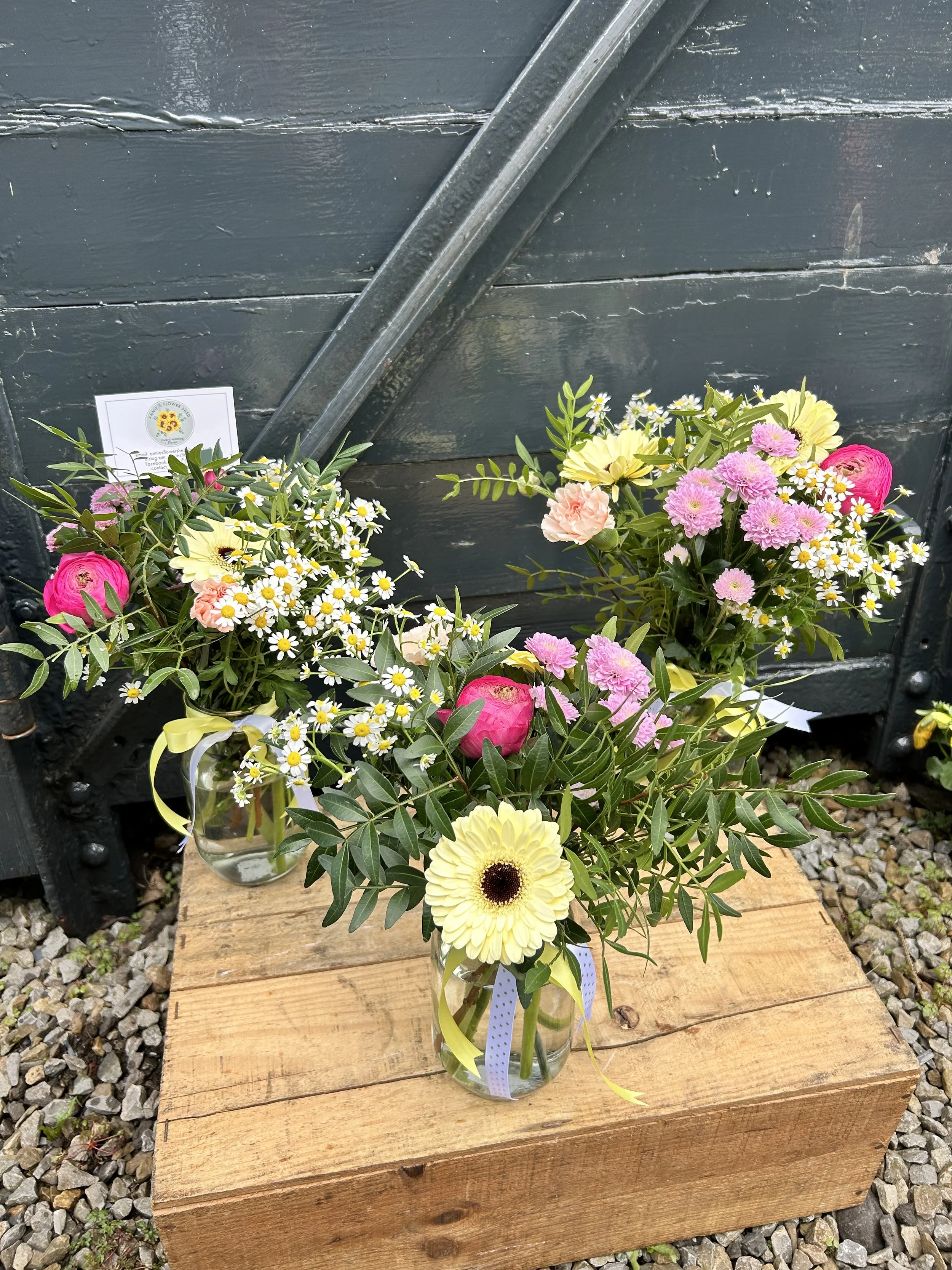 A bouquet of mixed colorful flowers in a glass vase on a wooden surface, with a dark gray background.