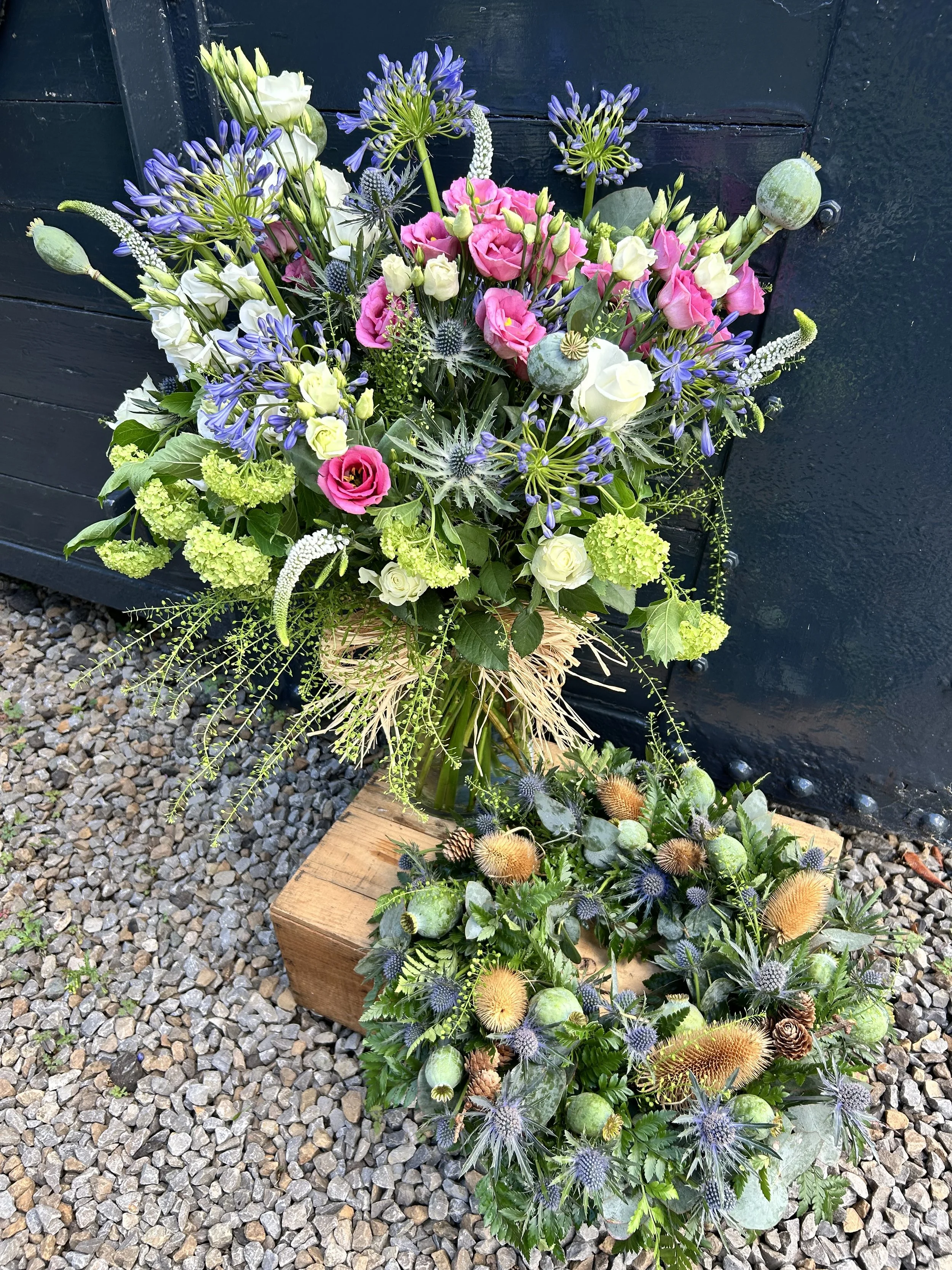Colourful arrangement of mixed flowers including pink roses, white roses, purple agapanthus, blue thistles, displayed in vase