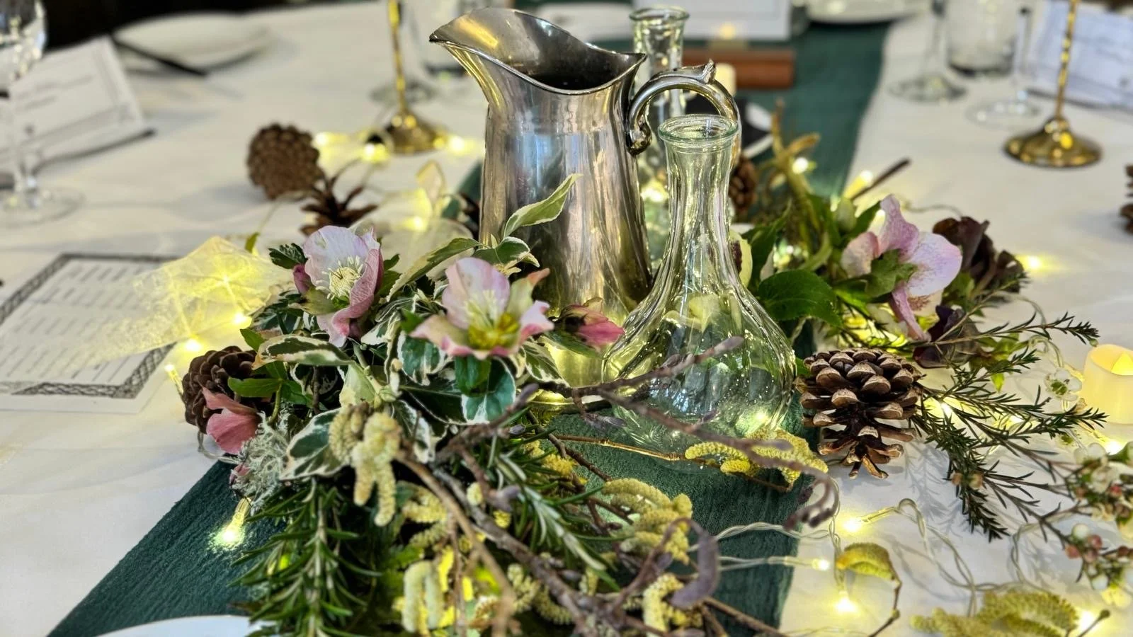 Decorative table centerpiece with pink and white flowers, pinecones, greenery.