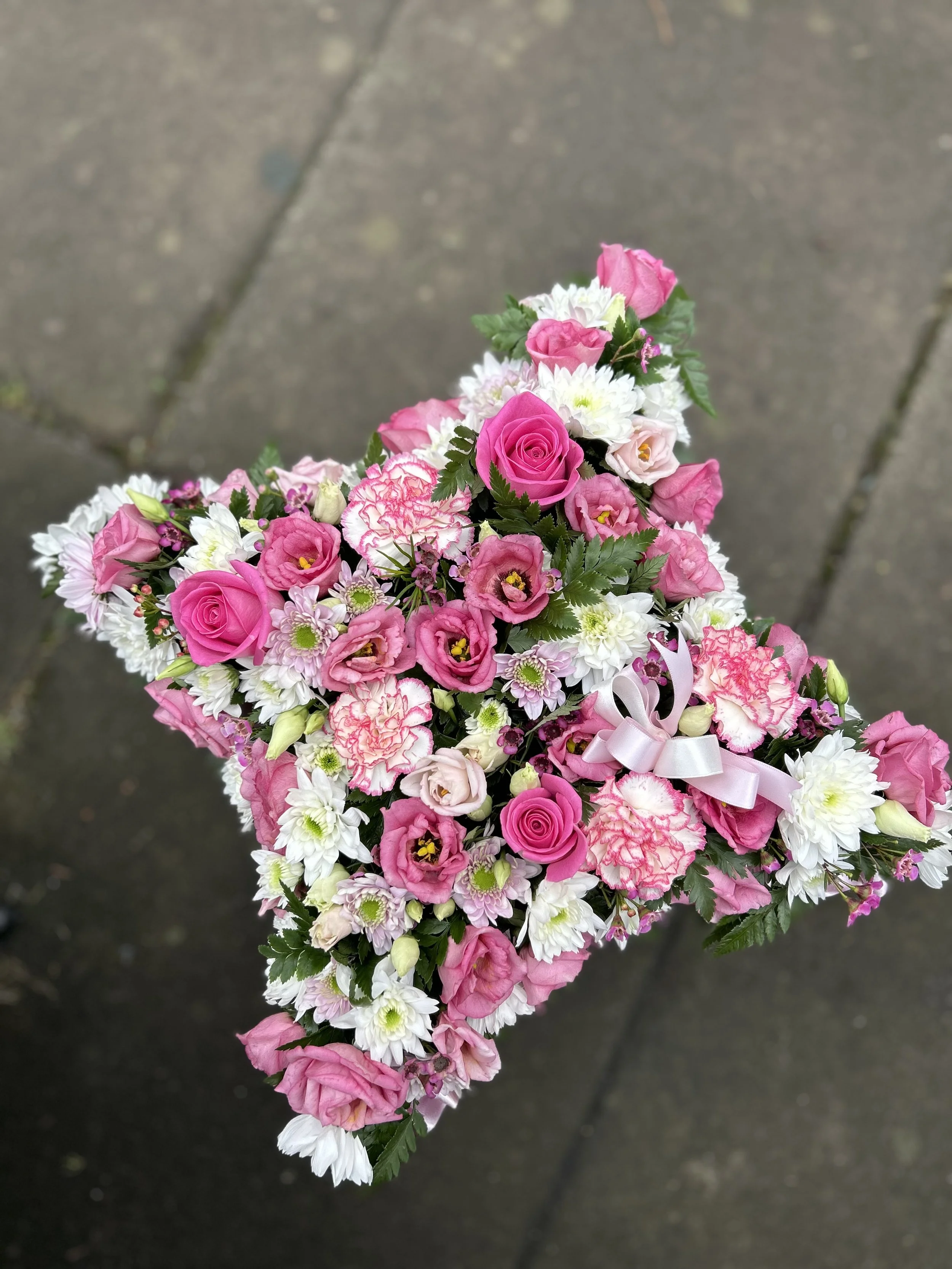 A bouquet of pink and white flowers including roses and chrysanthemums, with green leaves, held above a concrete pavement.