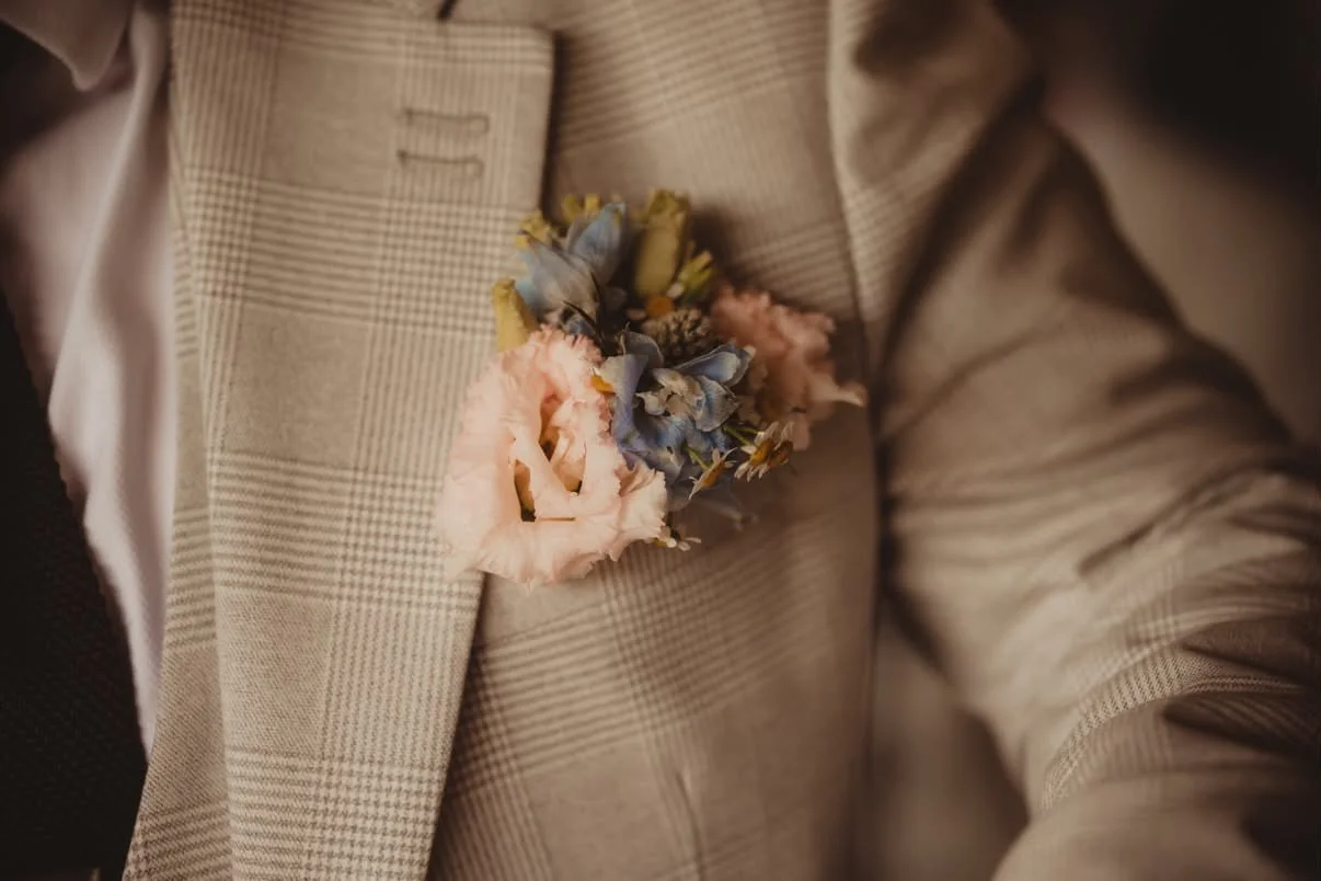 Close-up of a beige checkered suit jacket with a pink and blue floral boutonniere pinned to the lapel.