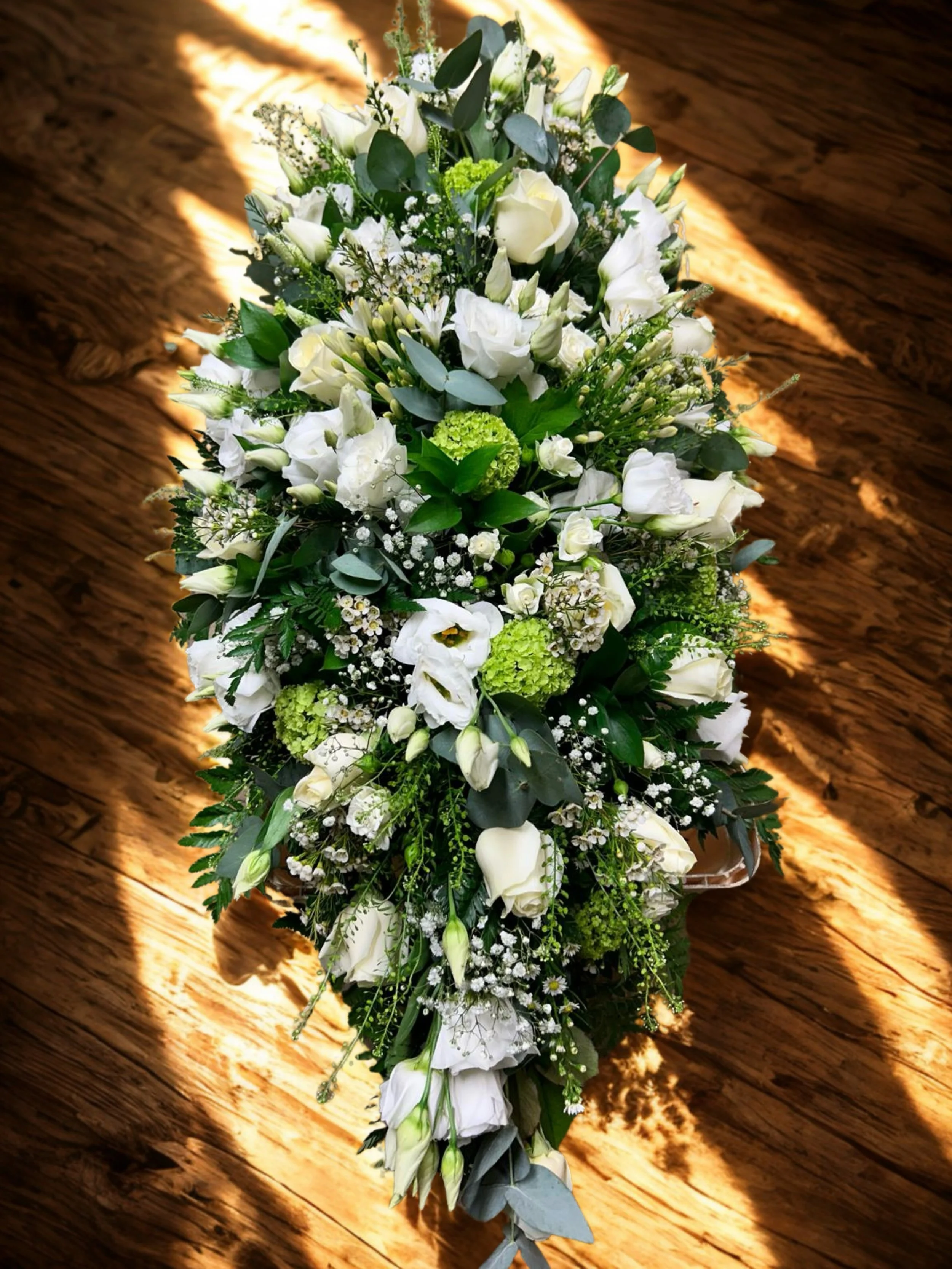 A white floral arrangement on a wooden surface illuminated by warm sunlight.