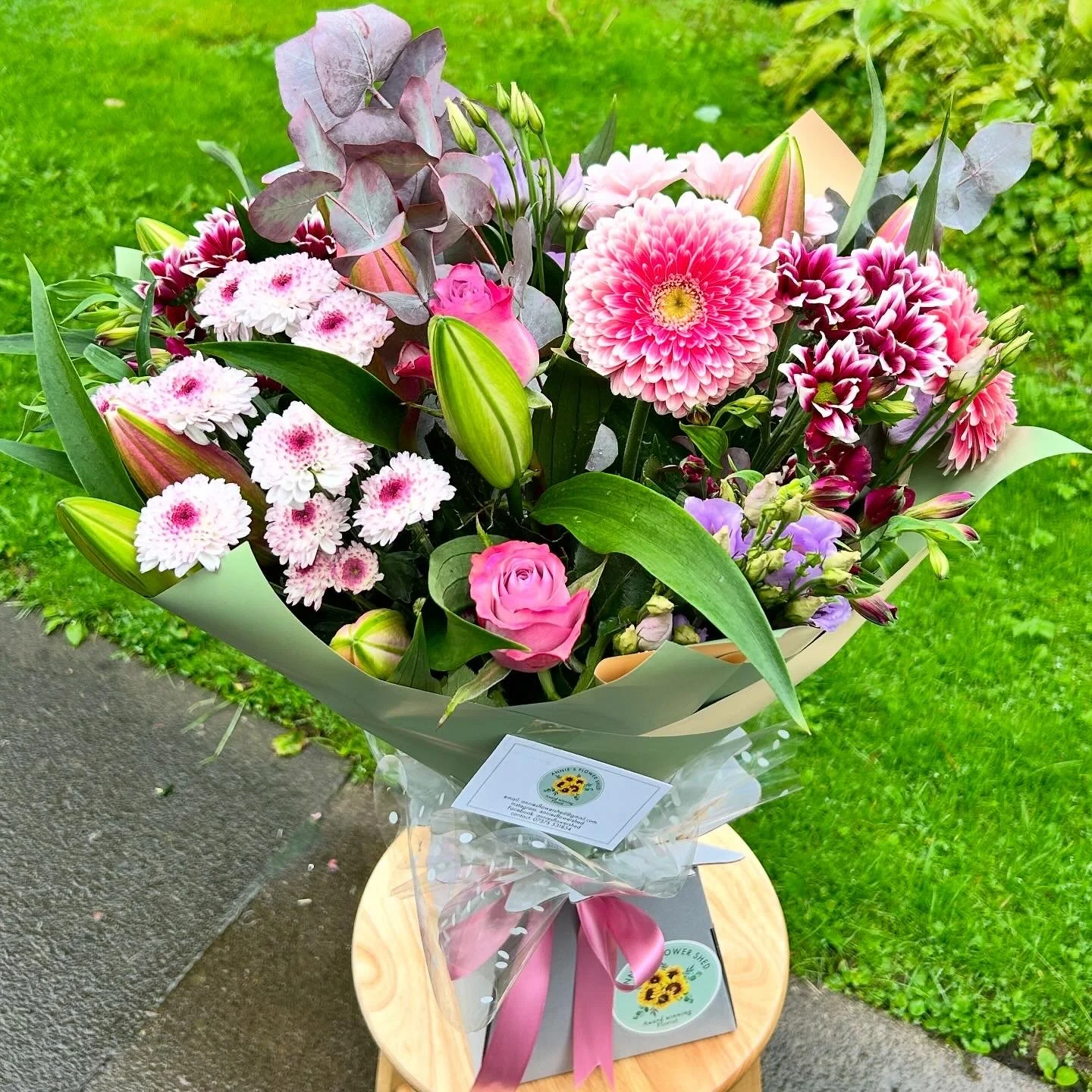 A colorful bouquet of pink and purple flowers on a wooden table, outdoors on a grassy area.
