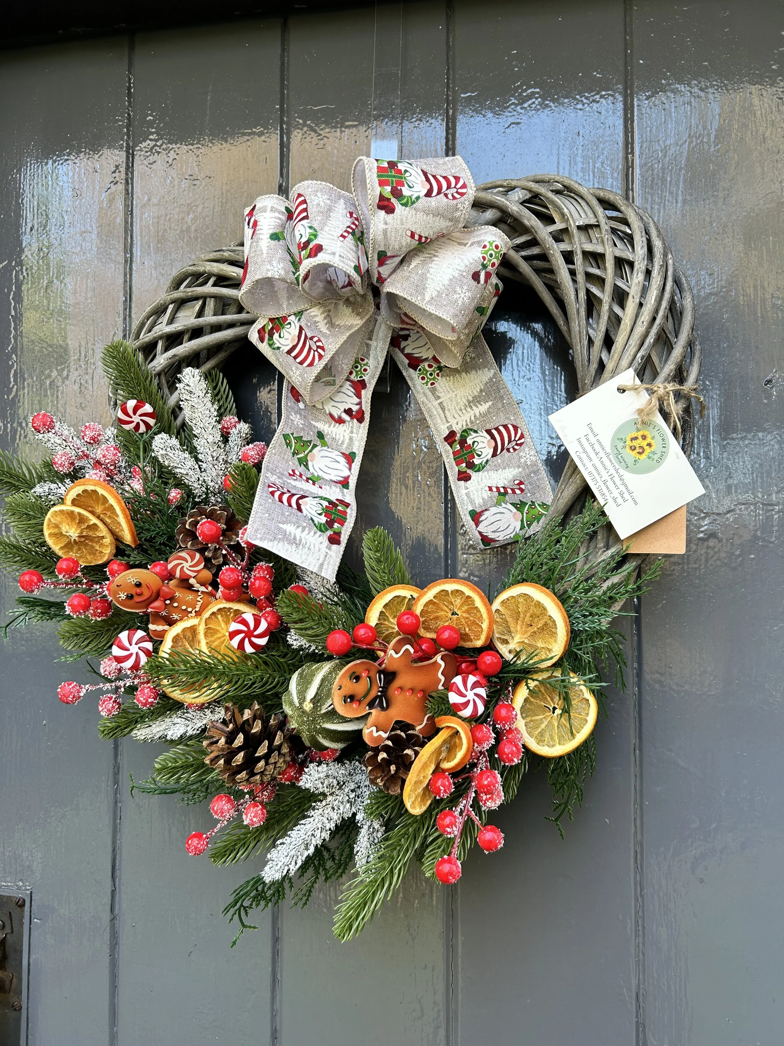 Christmas wreath decorated with pine branches, dried orange slices, pine cones, red berries, peppermint candies, gingerbread cookies, and a large bow with holiday patterns.