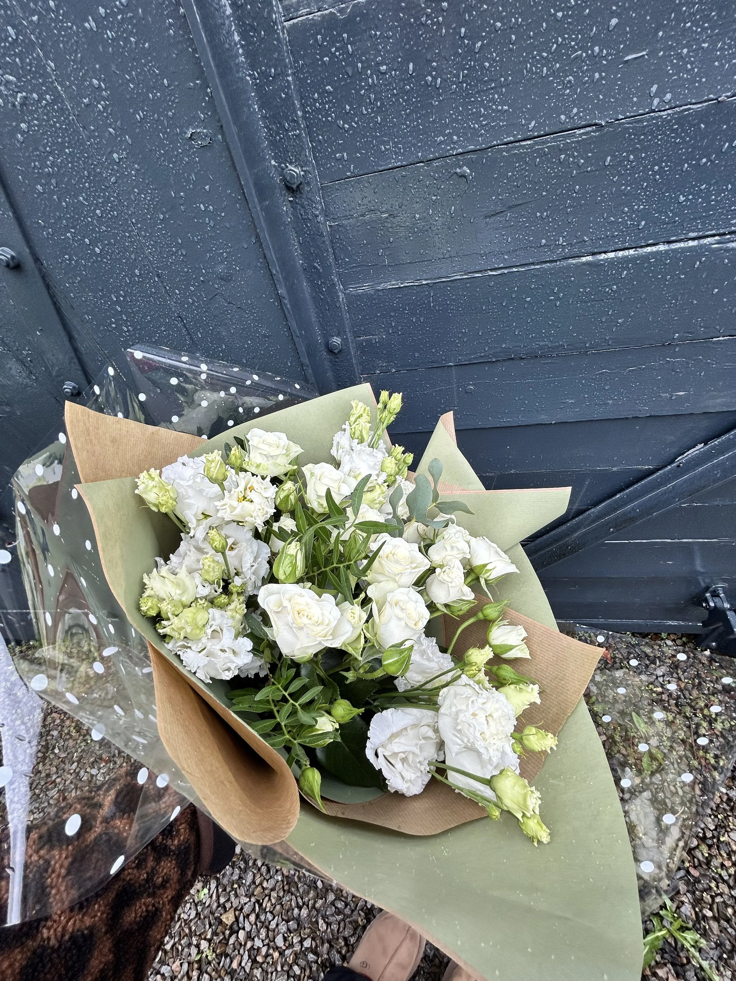 Bouquet of white flowers wrapped in brown and green paper resting on a black surface with a blue wooden wall in the background.