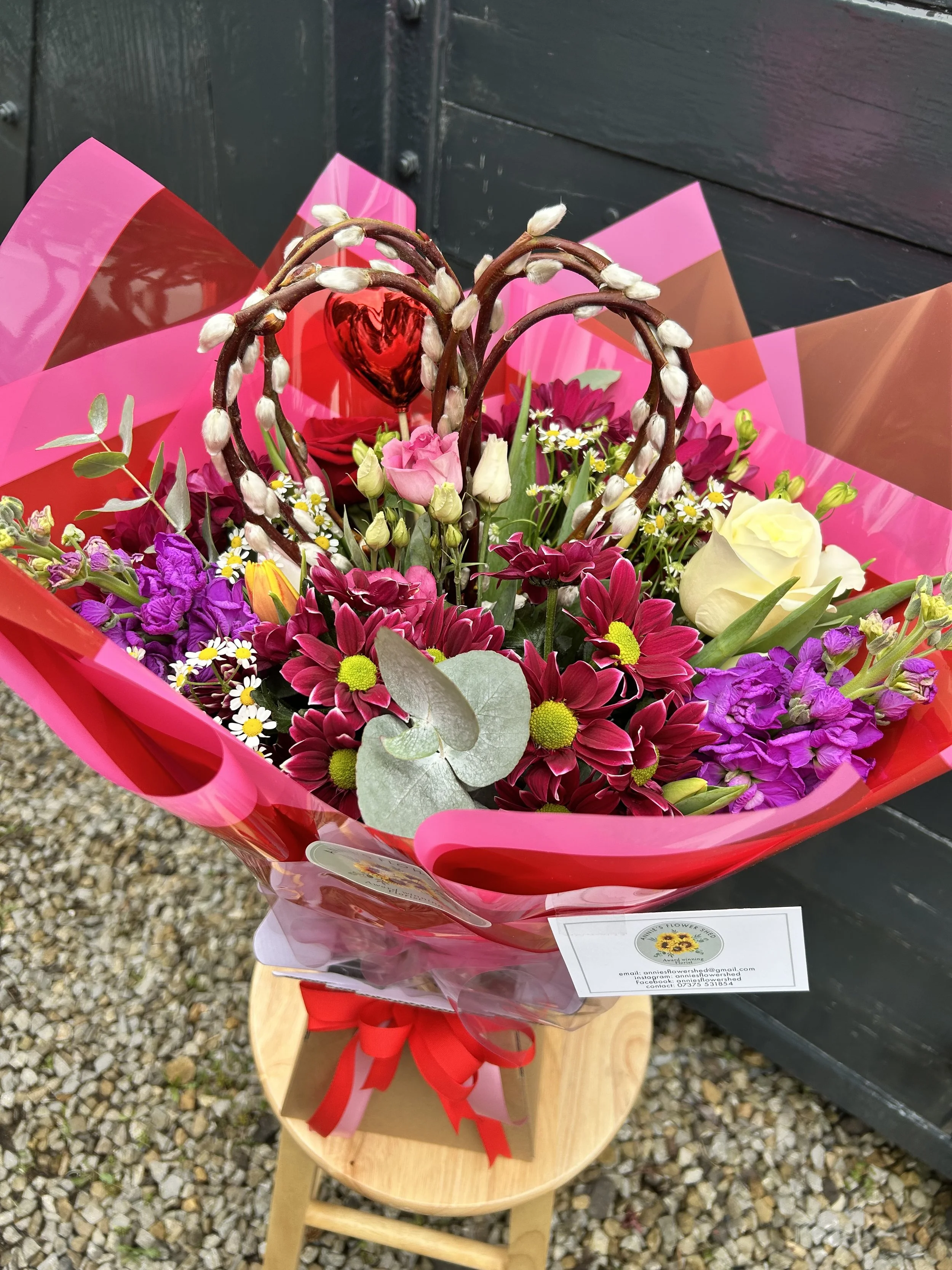Colorful bouquet of flowers with pink, white, purple, and red blooms, wrapped in pink and red wrapping paper with a red ribbon.