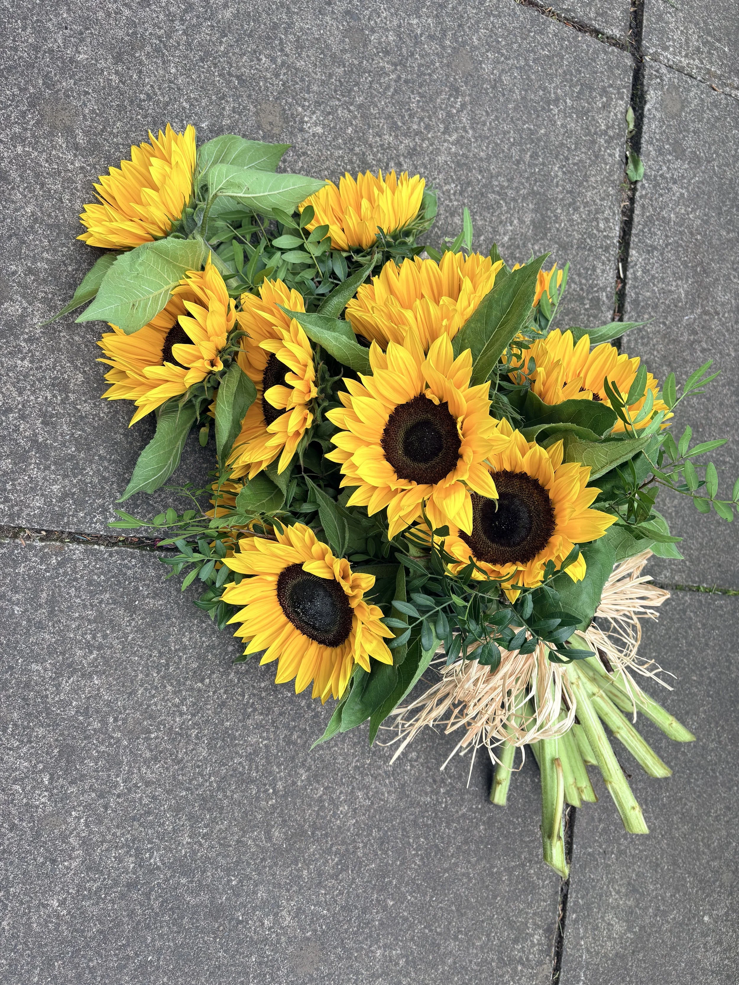 A bouquet of sunflowers with green leaves resting on a gray concrete surface.
