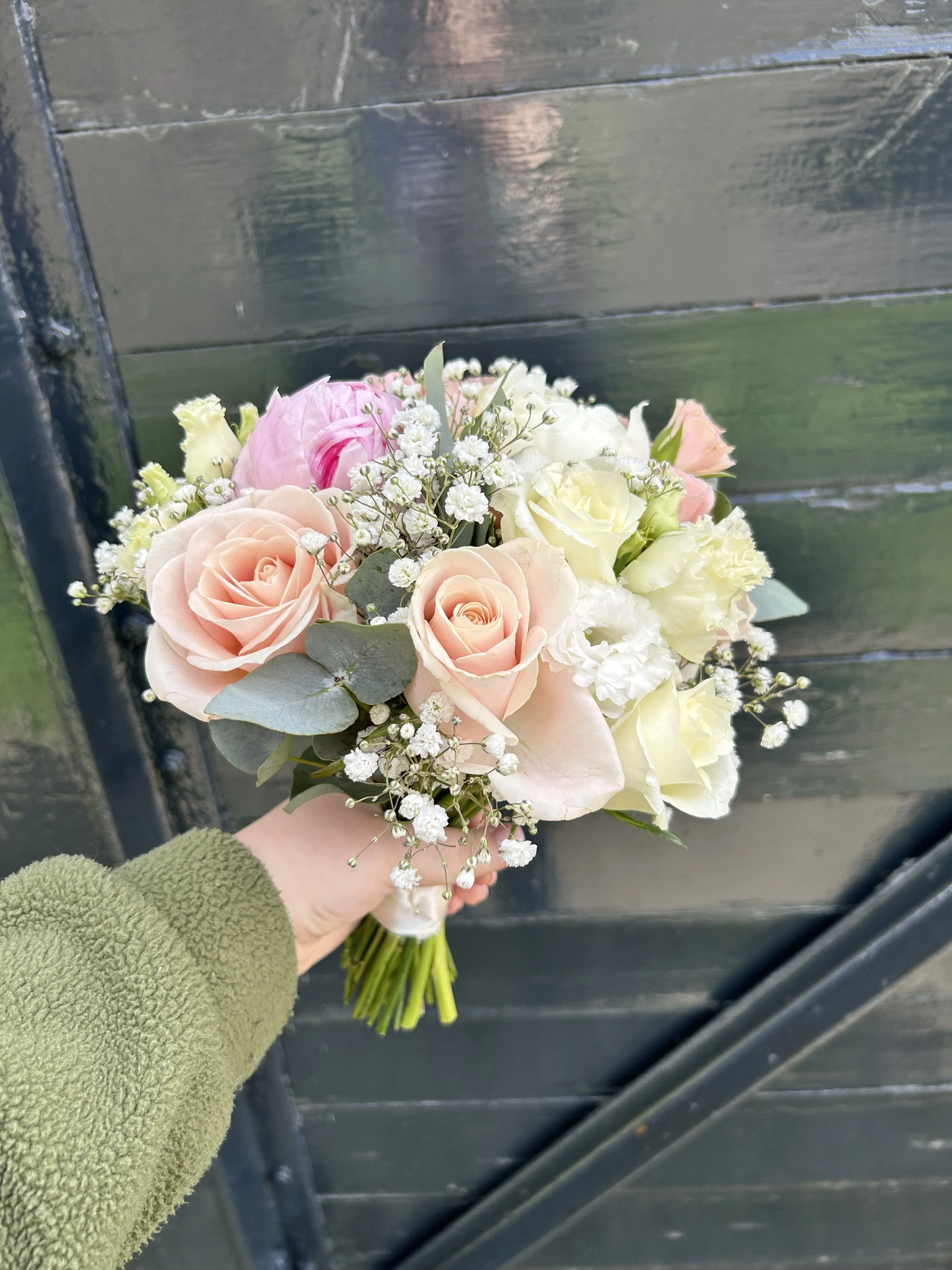 A person holding a bouquet of flowers outdoors, with a black wooden fence in the background.