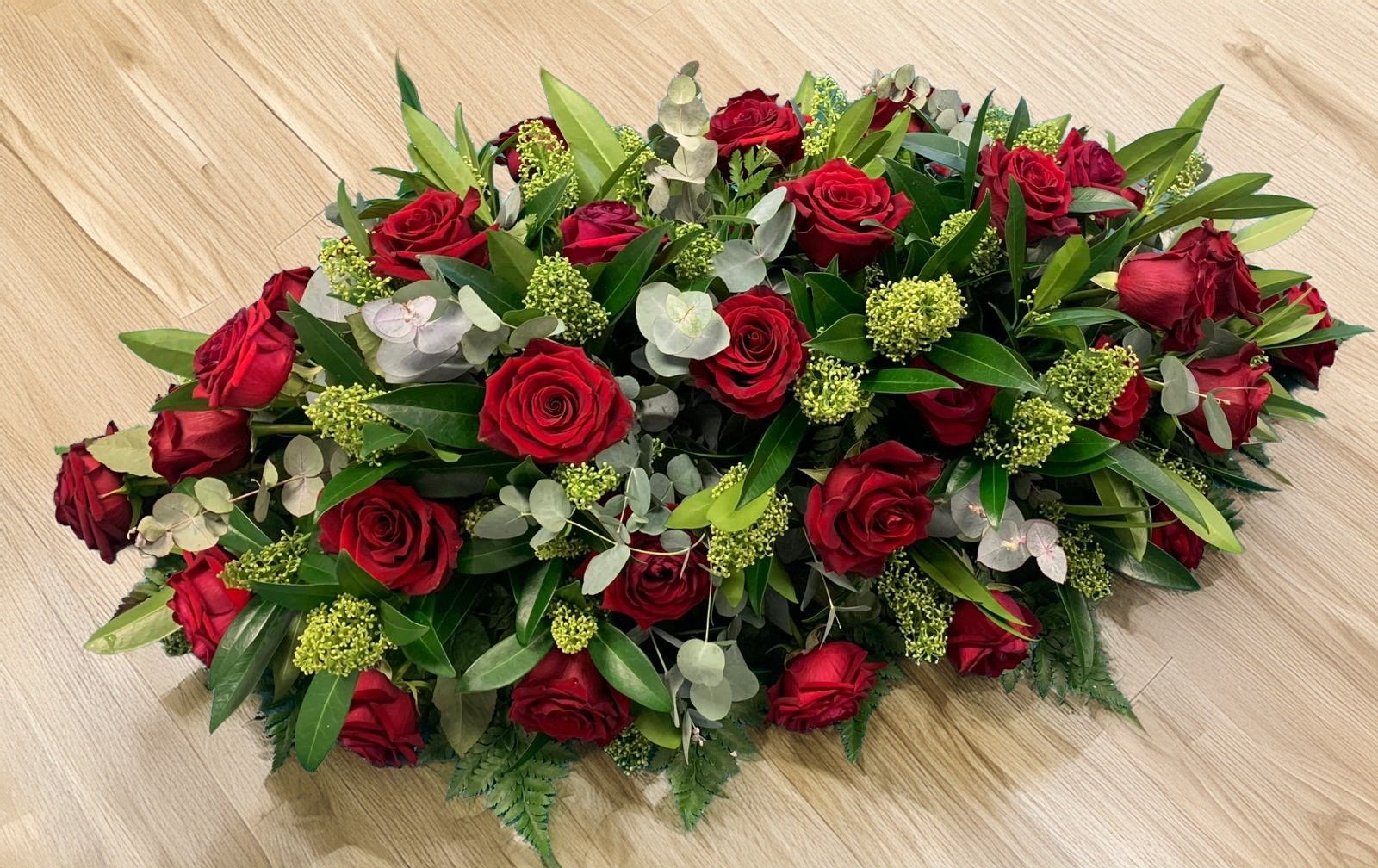 A floral arrangement with red roses, green foliage, and small green flowers on a wooden surface.