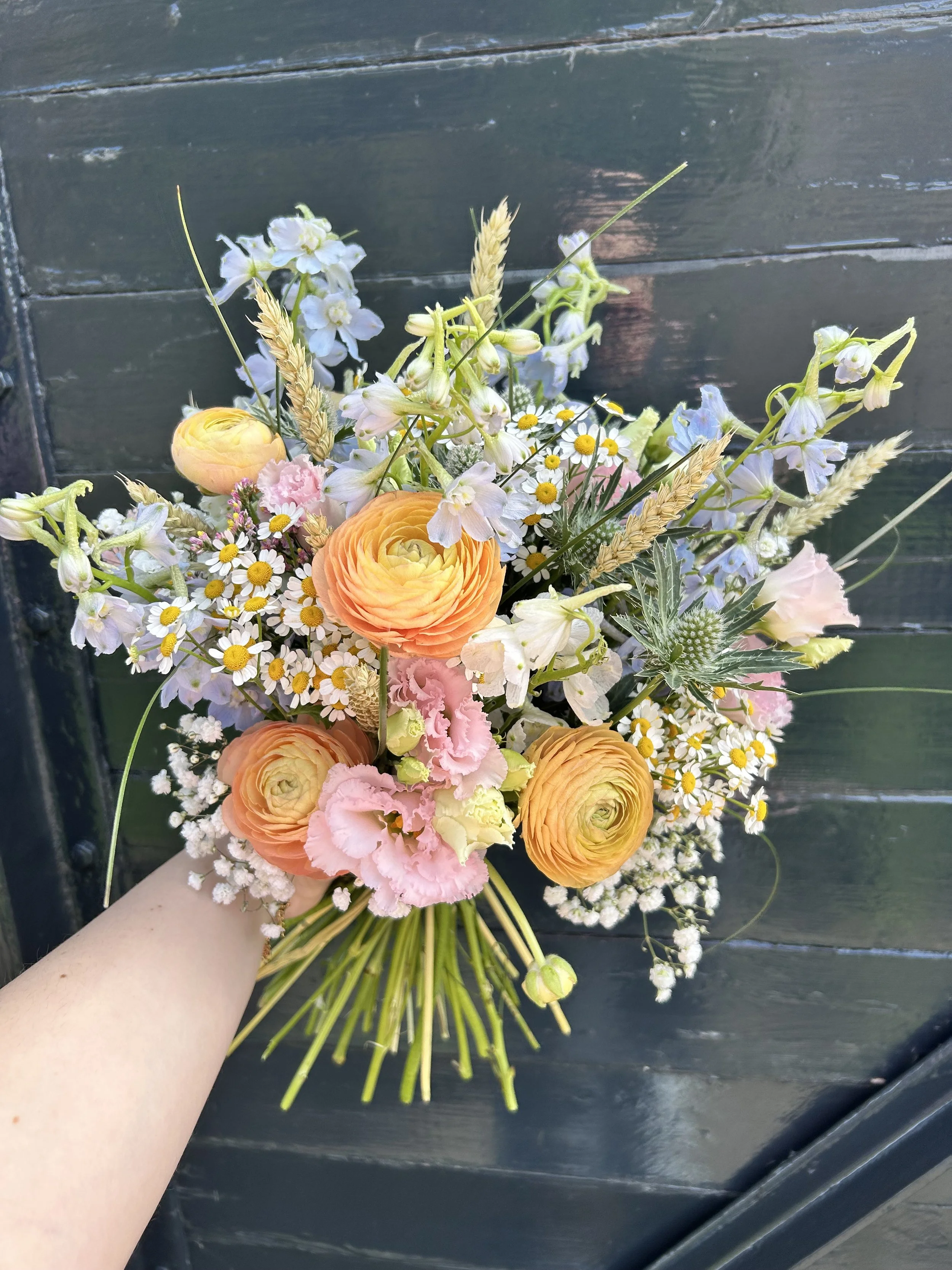 A person's arm holding a bouquet of mixed flowers against a dark, wooden background.