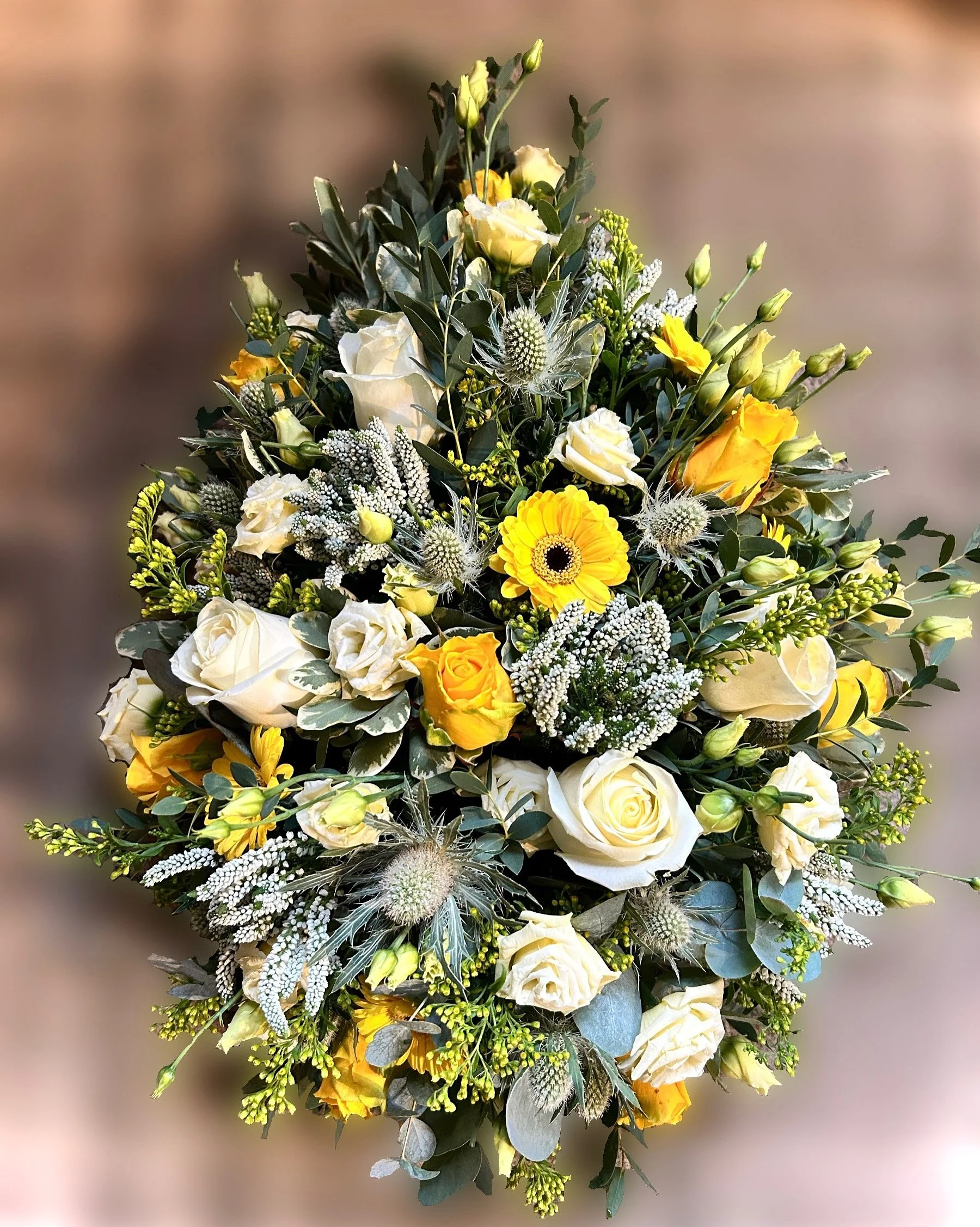 A bouquet of cream and yellow roses, white baby's breath, yellow gerbera daisies, green leaves, and textured thistles.