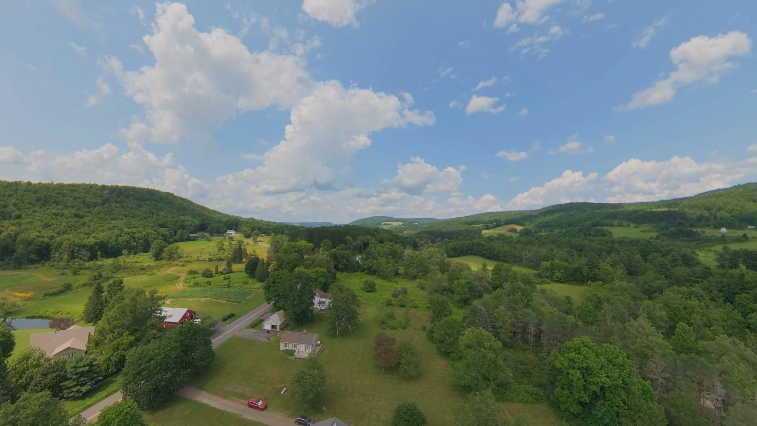 Aerial drone photograph showing panoramic views of green countryside, rolling hills, and scattered residential properties, highlighting the surrounding landscape and location.
