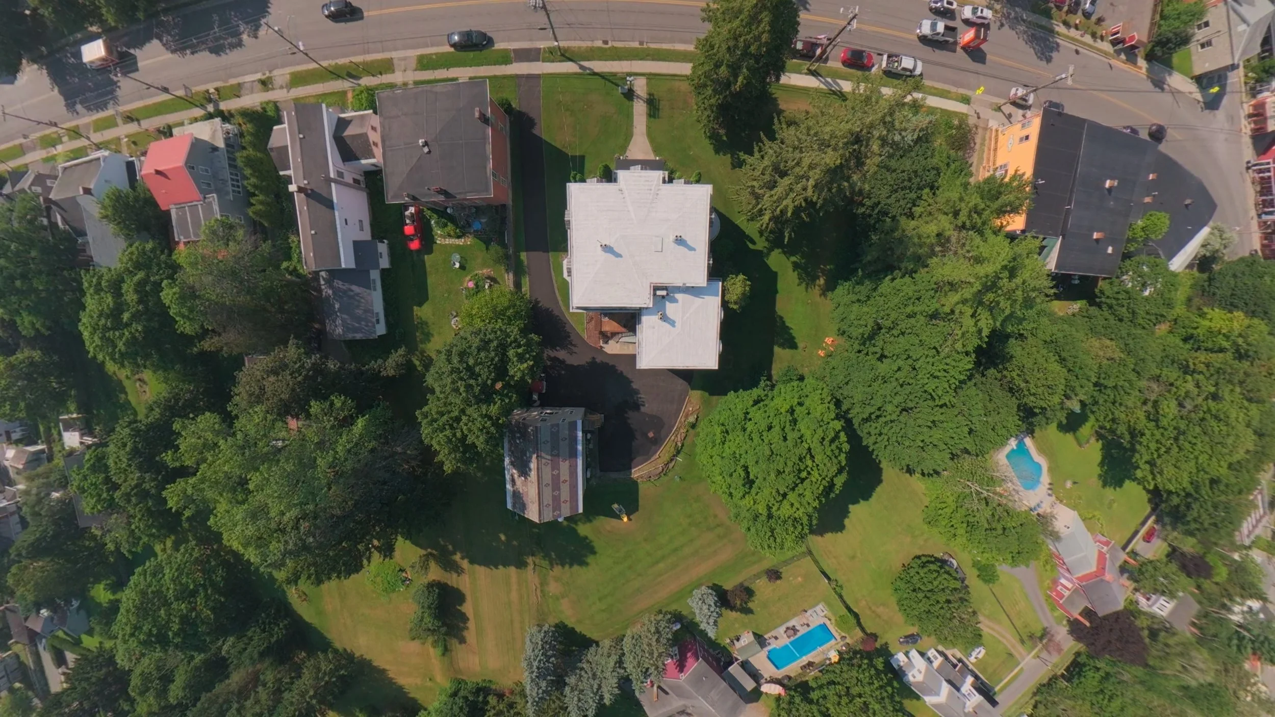 Top-down aerial drone photograph of a residential property, showcasing the building's roof, landscaped grounds, surrounding trees, and outdoor swimming pool.
