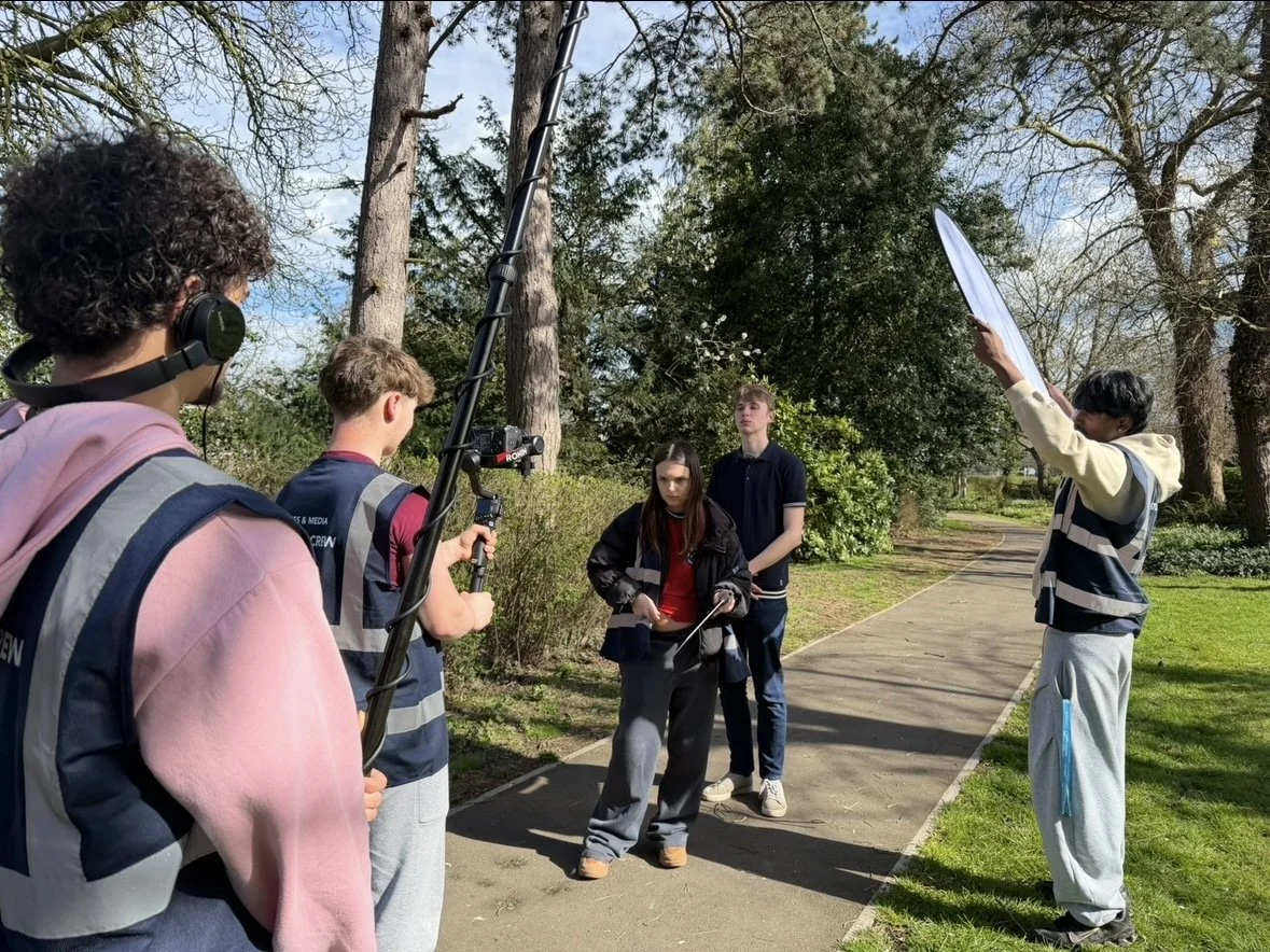 Group of teenagers filming a scene in a park with cameras and equipment.