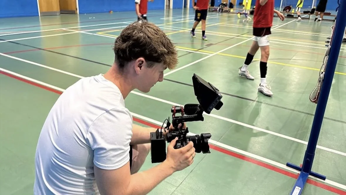 A person filming a volleyball game in an indoor gym using a camera on a stabilizer.