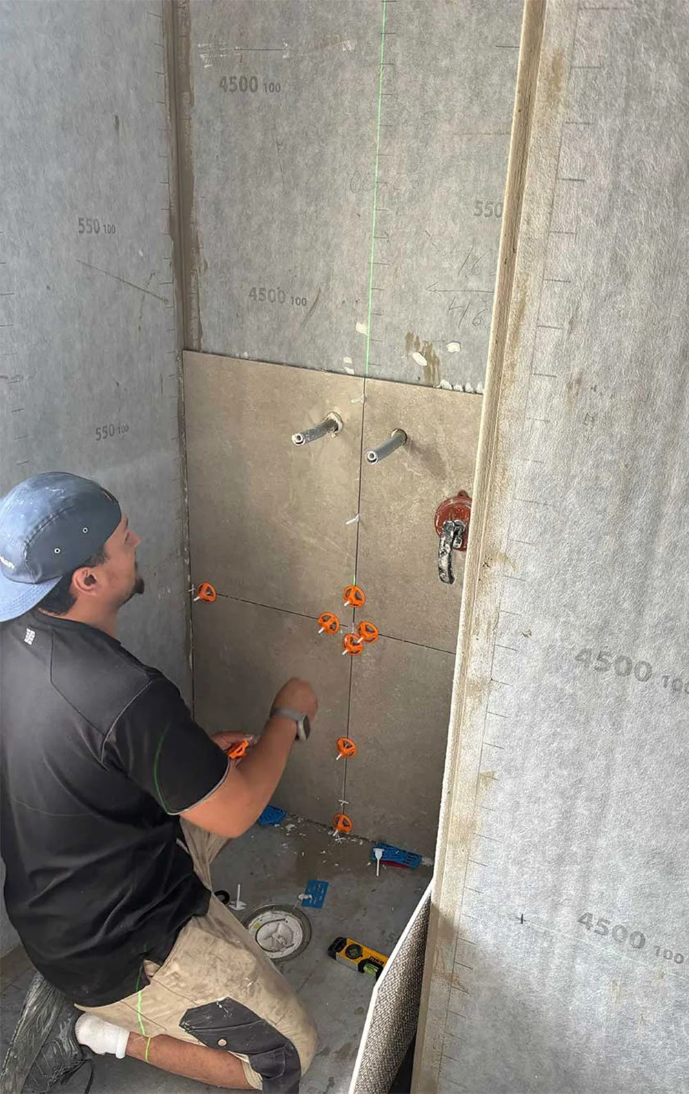 En person installerar rör i en vägg under en byggarbetsplats. Väggarna är isolerade och har mätlinjer och markeringar.