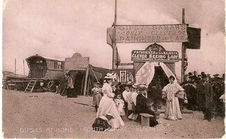 Victorian photo of South Shore gypsies in Blackpool approx. 1890s. Sign reads: "Gipsy Sarah's only clever daughter in law". Four Victorian women in white dresses and hats sit on a bench outside the tent under the sign waiting for the fortuneteller
