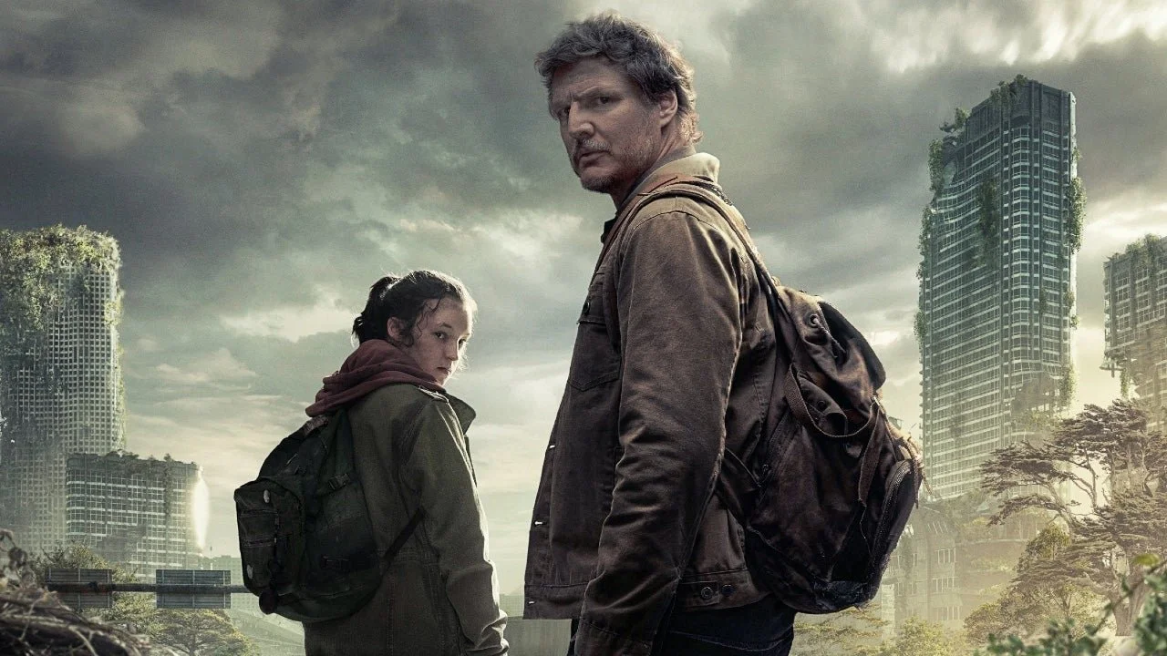 A 50 year old man stands sideways on wearing a tired brown jacket and backpack; he's dusty and frowning looking back at us. To his left is a teenage girl with brown hair looking back over her shoulder at us. Behind is an apocalyptic city.