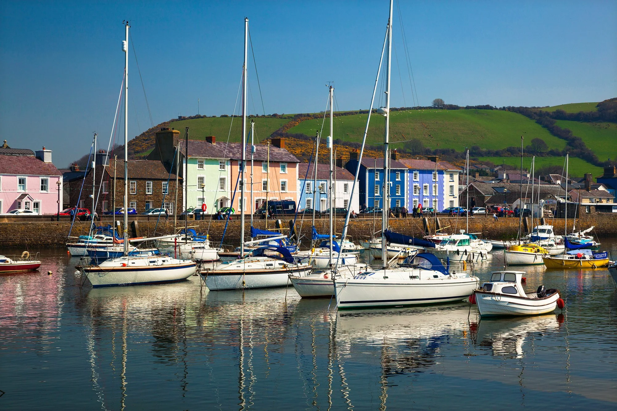 Small harbour full of boats in front of pastel coloured houses in Aberaeron, Wales.