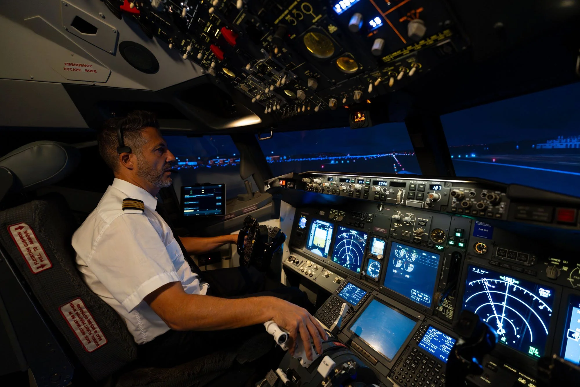 Piloto en la cabina de un avión durante la noche, rodeado de pantallas, controles y radios.