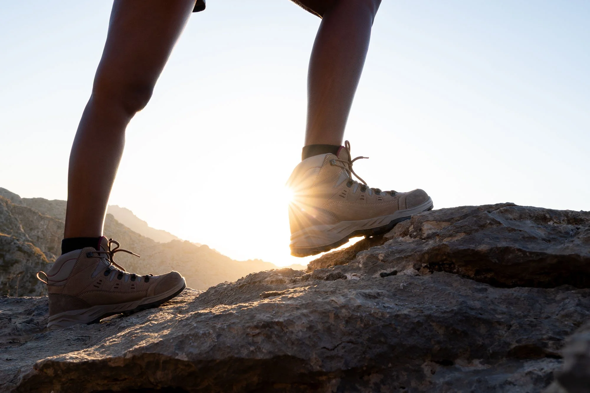 Personas con botas de senderismo caminando sobre rocas en una montaña al atardecer.